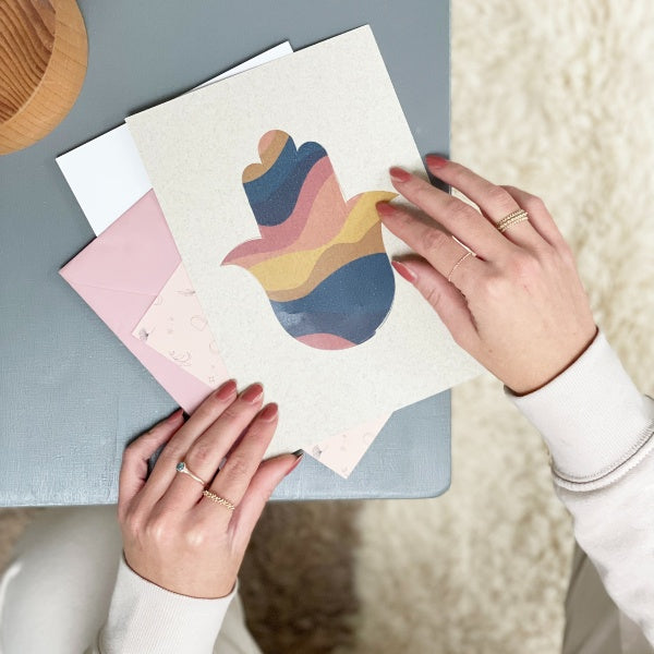 Mains feuilletant des cartes illustrées avec la khmissa de Casa Amar