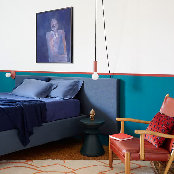 Chambre au mur bleu canard, lit bleu, fauteuil rouge et tapis ivoire à motifs orange