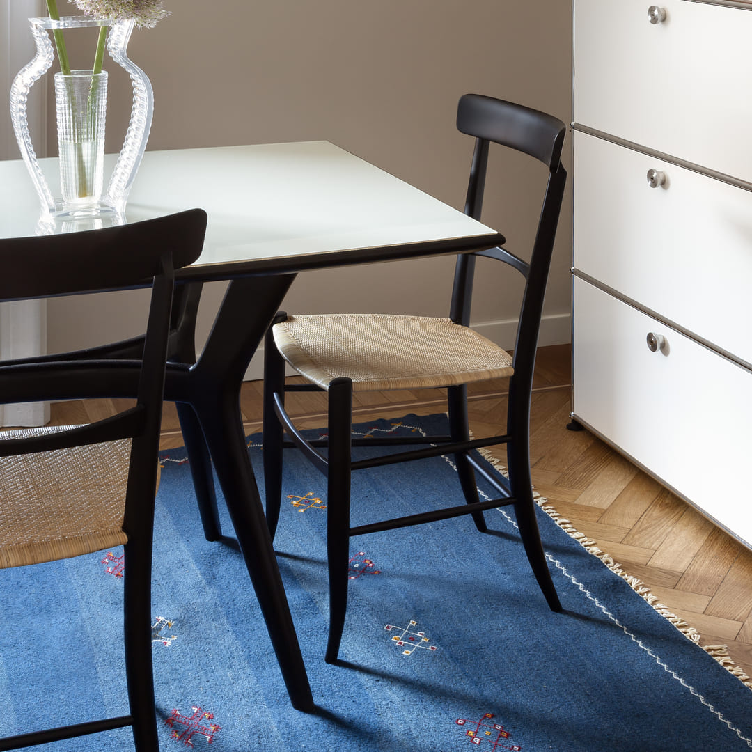 Table à manger blanche et chaises noires sur un tapis bleu tissé à plat orné de petits symboles
