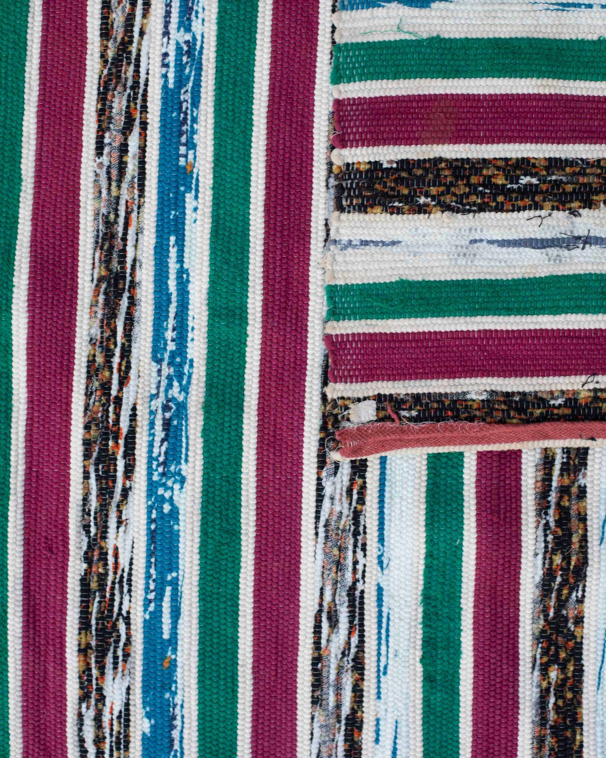Dettaglio della passatoia di stracci Boucherouite in tessuti misti riciclati a righe ciclamino, verdi, azzurre, bianche, nere