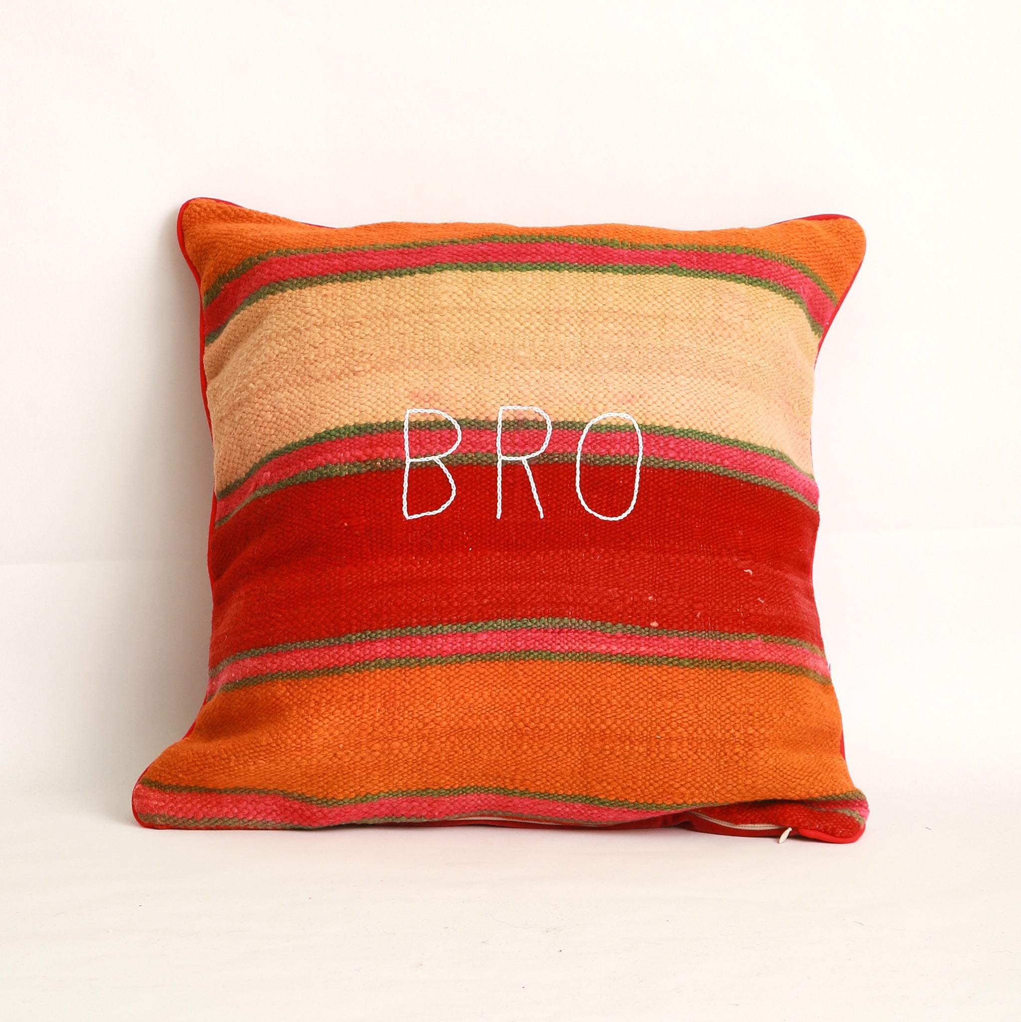 Copricuscino realizzato con 2 tessuti, uno diverso da ogni lato. Sul lato mostrato, coperta vintage tessuta a mano in Marocco, a righe colorate arancione rosso rosa e verde acqua, ricamo a mano con la parola Bro, bordo tutto attorno al cuscino piping in cotone rosso grande