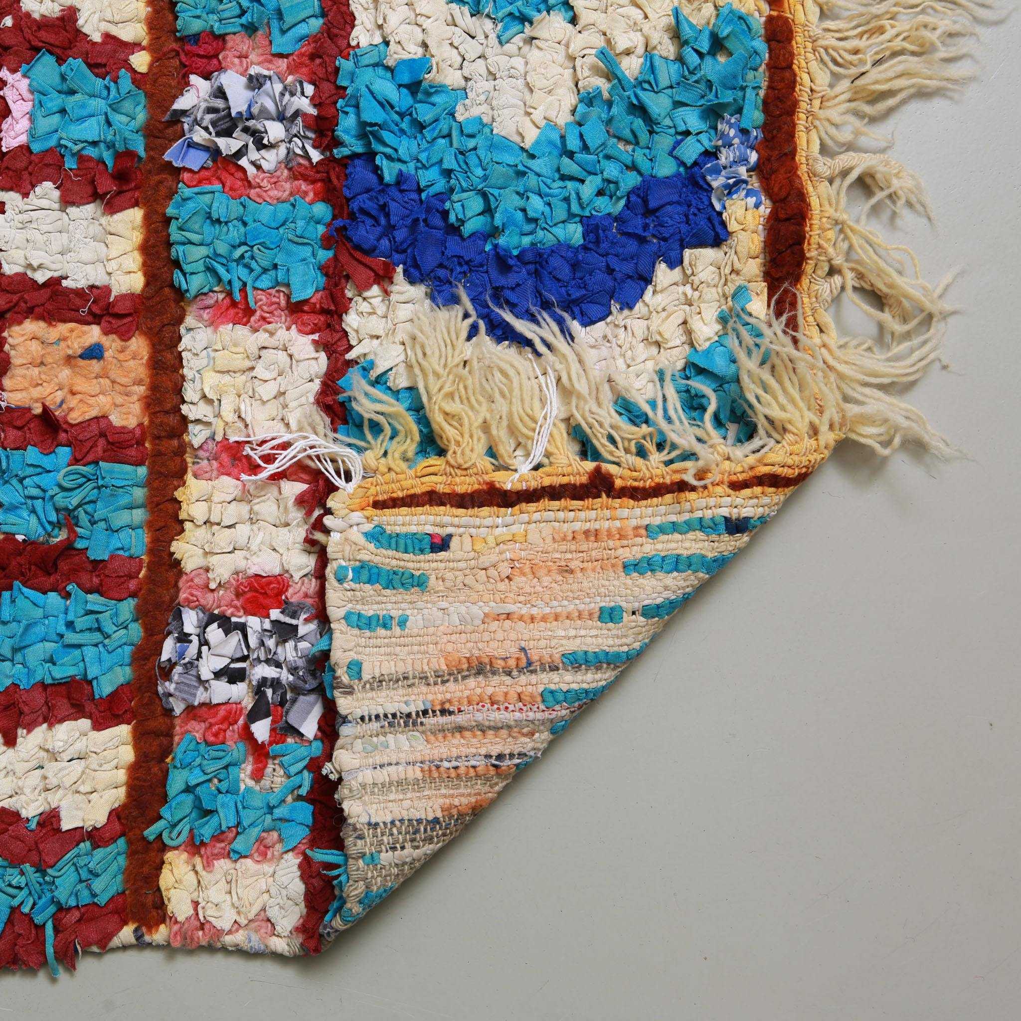 Dettaglio del retro dell'angolo e della frangia di un tappeto Boucherouite artigianale marocchino con tessuti riciclati dai colori blu azzurro blu bianco e righe rosse