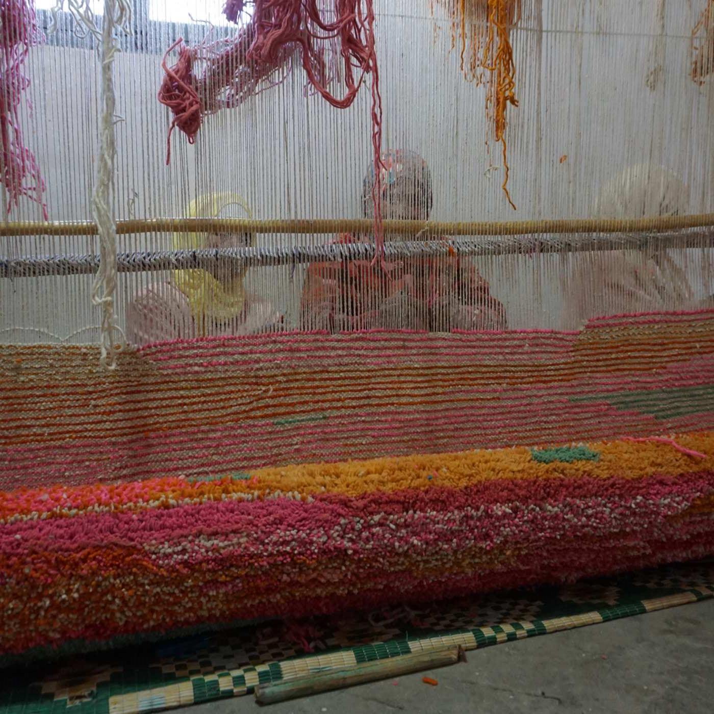 tre artigiane marocchine che lavorano dietro a un telaio mentre realizzano un tappeto