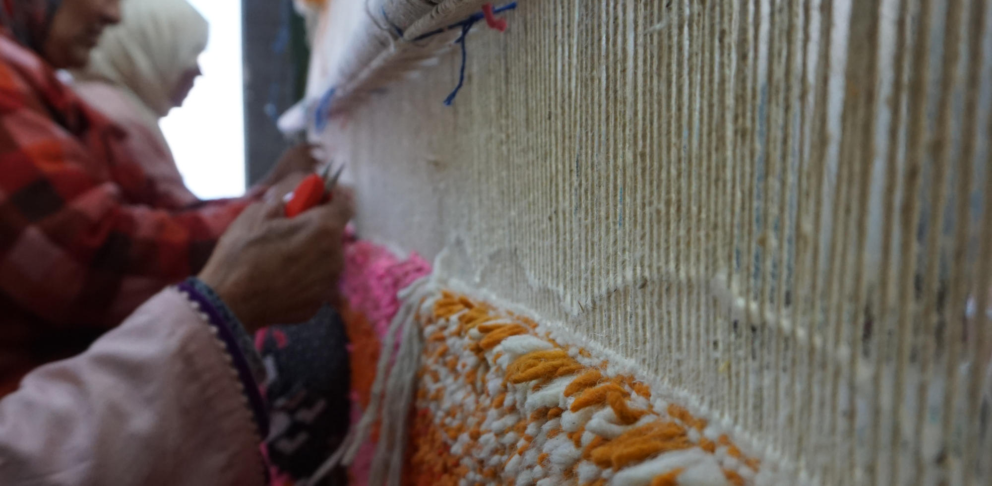 Nouage traditionnel d'un tapis marocain (couramment appelé berbère). Gros plan sur les mains expertes de l'artisane travaillant la laine pure, créant des motifs géométriques selon la tradition ancestrale de l'Atlas.