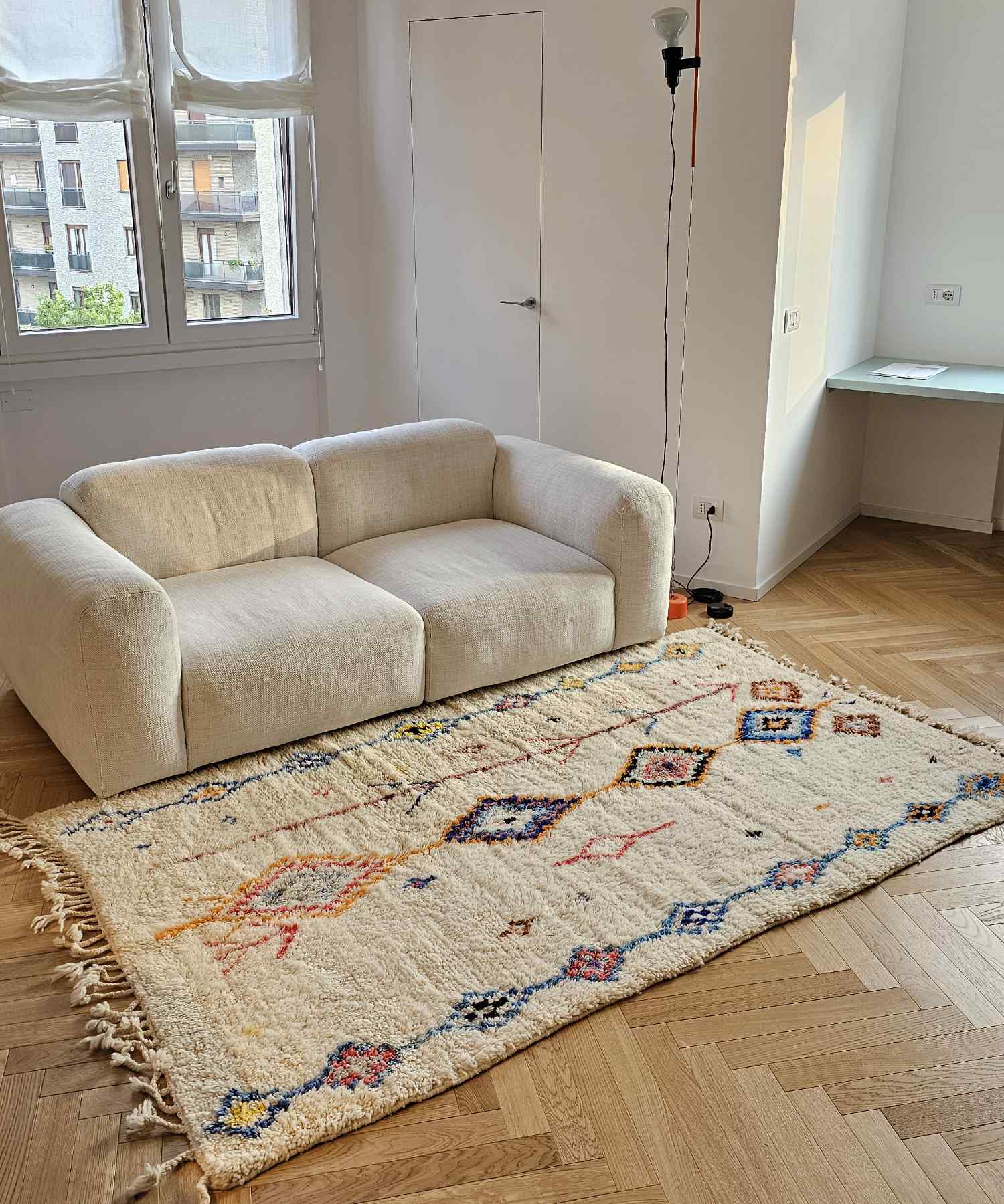 Tappeto Azilal avorio con motivi geometrici colorati ideale per questo salotto in stile moderno, minimal, contemporaneo e scandinavo, caratterizzato da divano beige e parquet a spina di pesce