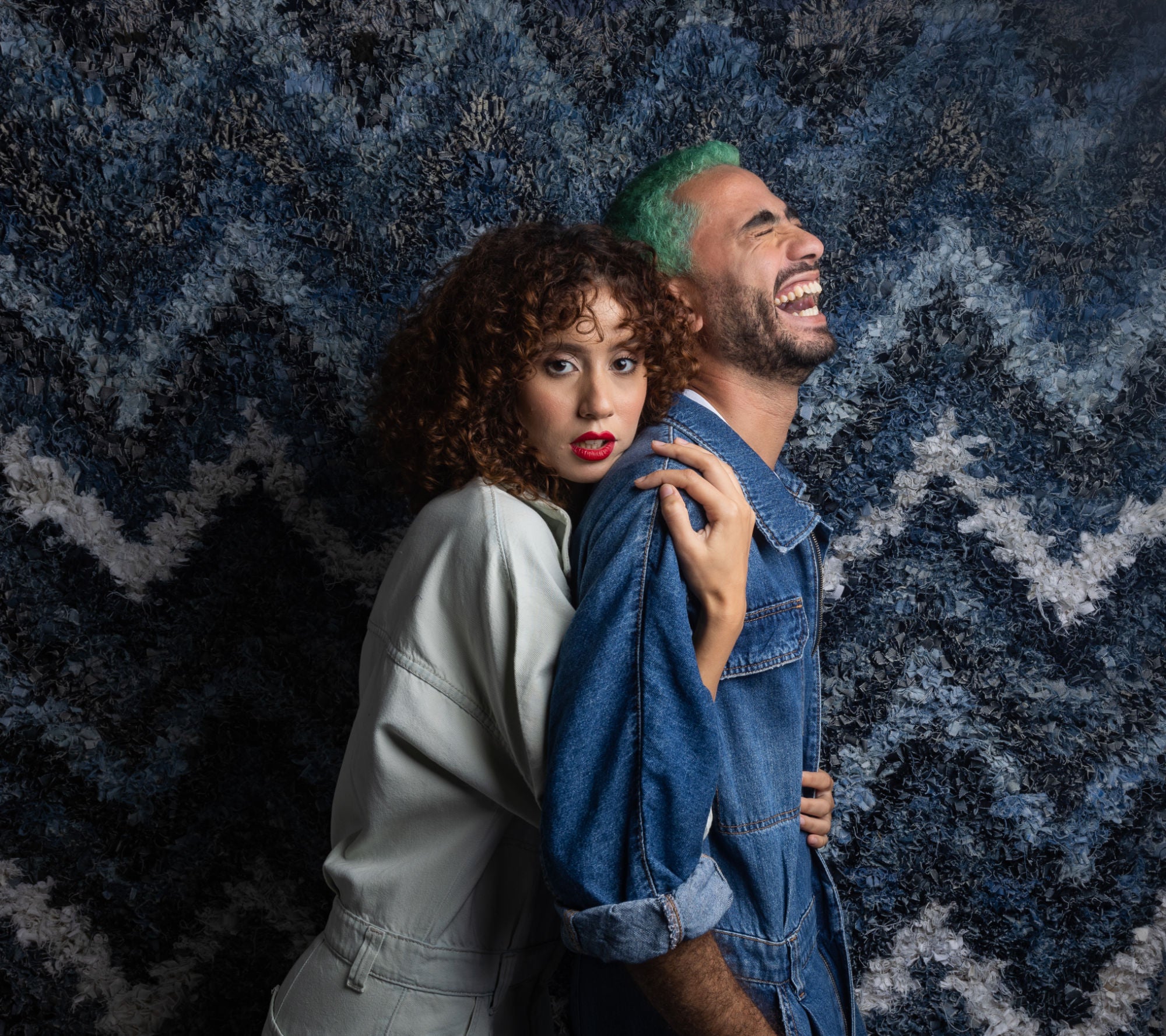 ragazzo e ragazza con salopette in jeans abbracciati con sfondo un tappeto boucherouite in denim a zig zag