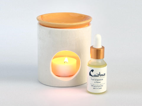 diffusore in ceramica bianco con piattino giallo con all'interno una candela accesa e alla destra un boccettina di olio profumato per la casa