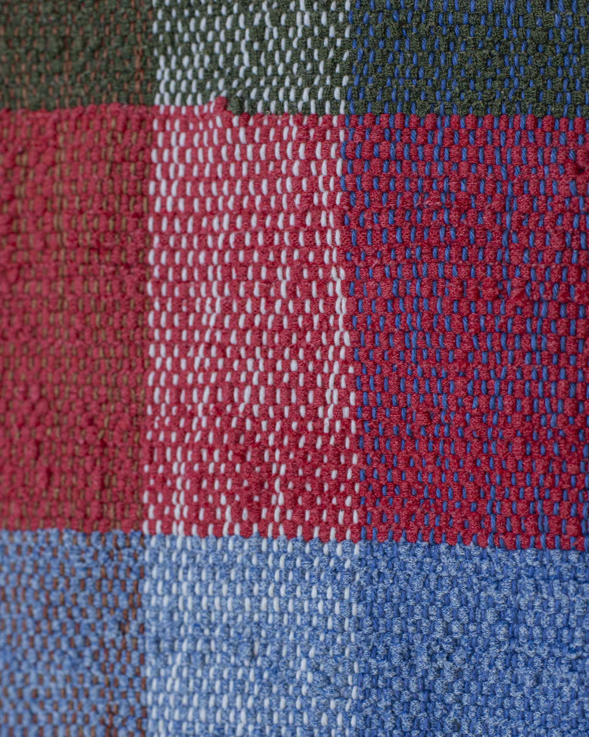 Dettaglio del copricuscino realizzato con filati misti di recupero nei colori rosso, blu, bianco, verde