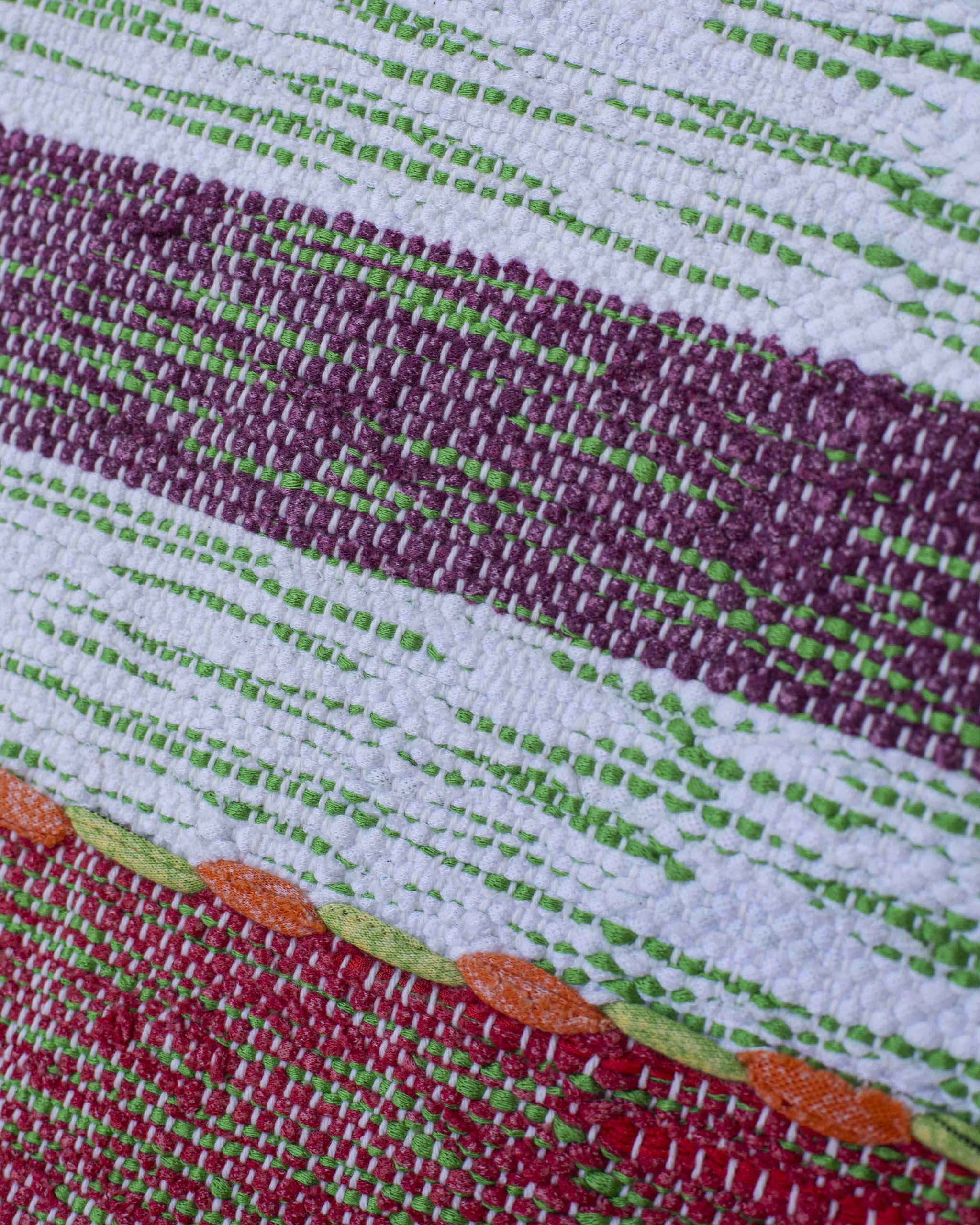 Dettaglio del tessuto del cuscino in filati melange rosso-verde, bianco-verde, viola-verde