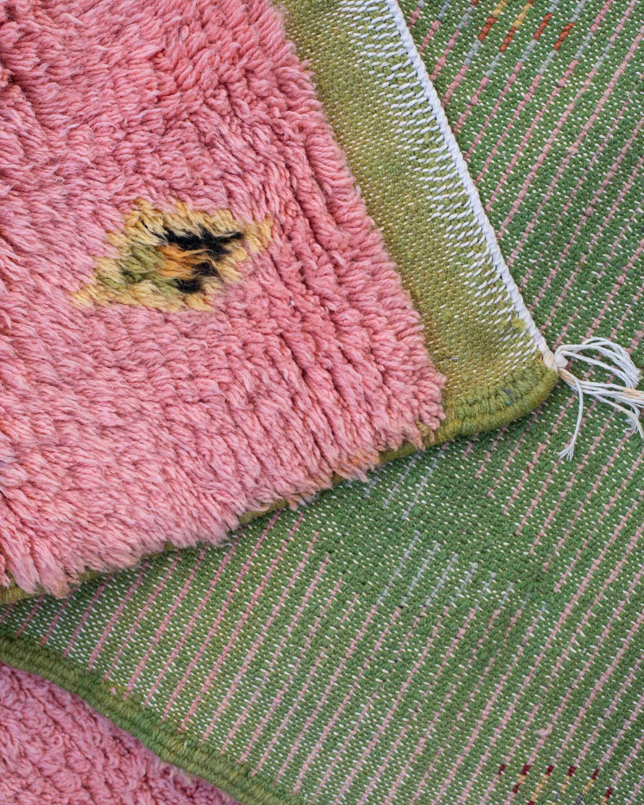 Dettaglio dritto-rovescio del tappeto in lana rosa e verde con simboli geometrici sparsi
