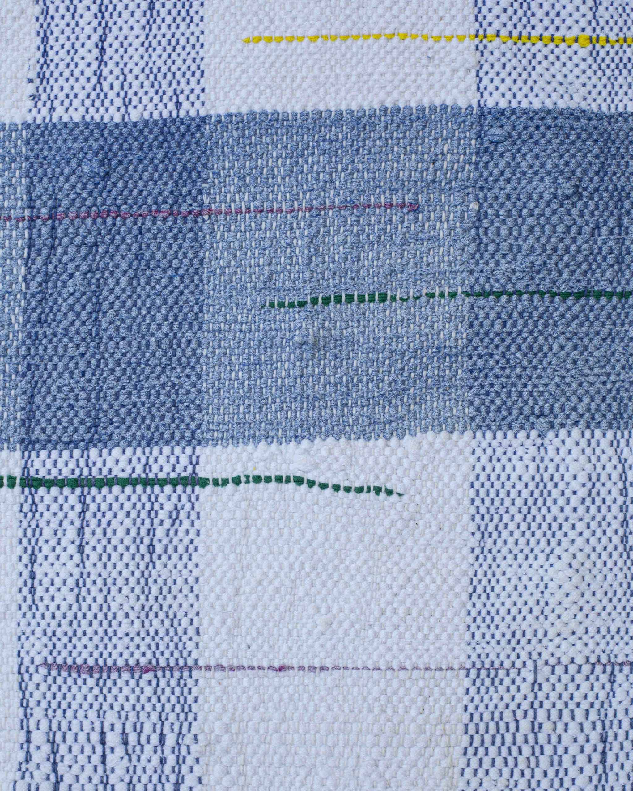 Dettaglio del tessuto fatto a mano con filati bianchi, azzurri, blu e righe sparse in giallo, rosso, verde