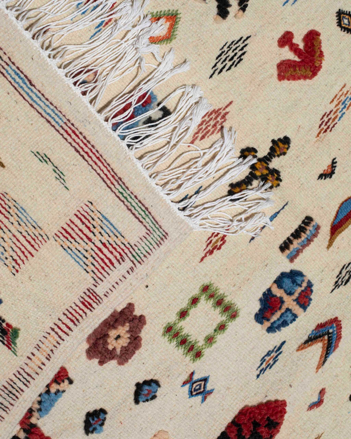Dettaglio delle frange e della tessitura piatta del kilim marocchino in lana naturale con simboli colorati