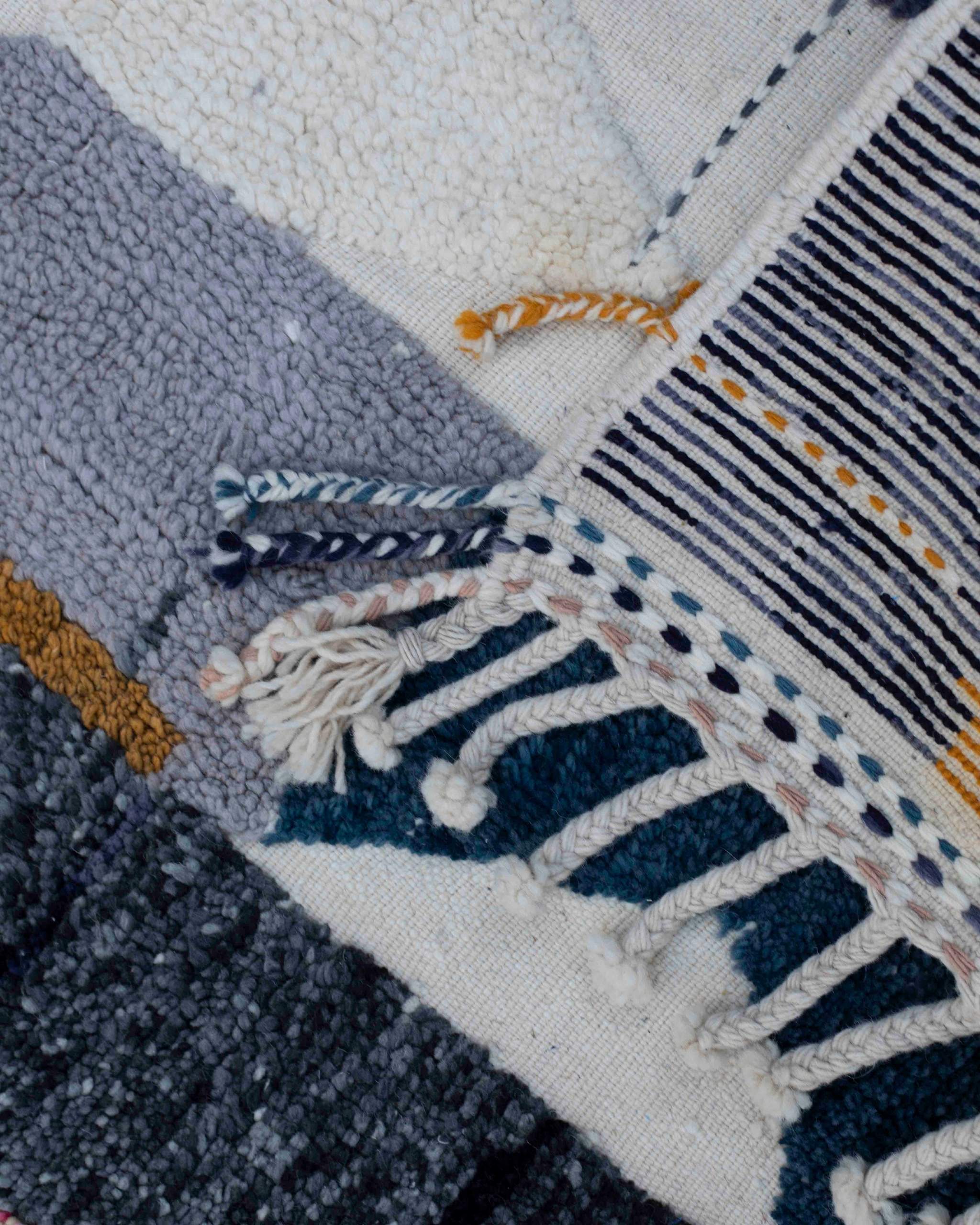 Dettaglio angolo tappeto in lana a tessitura mista con frange intrecciate e cordoncini decorativi in lana