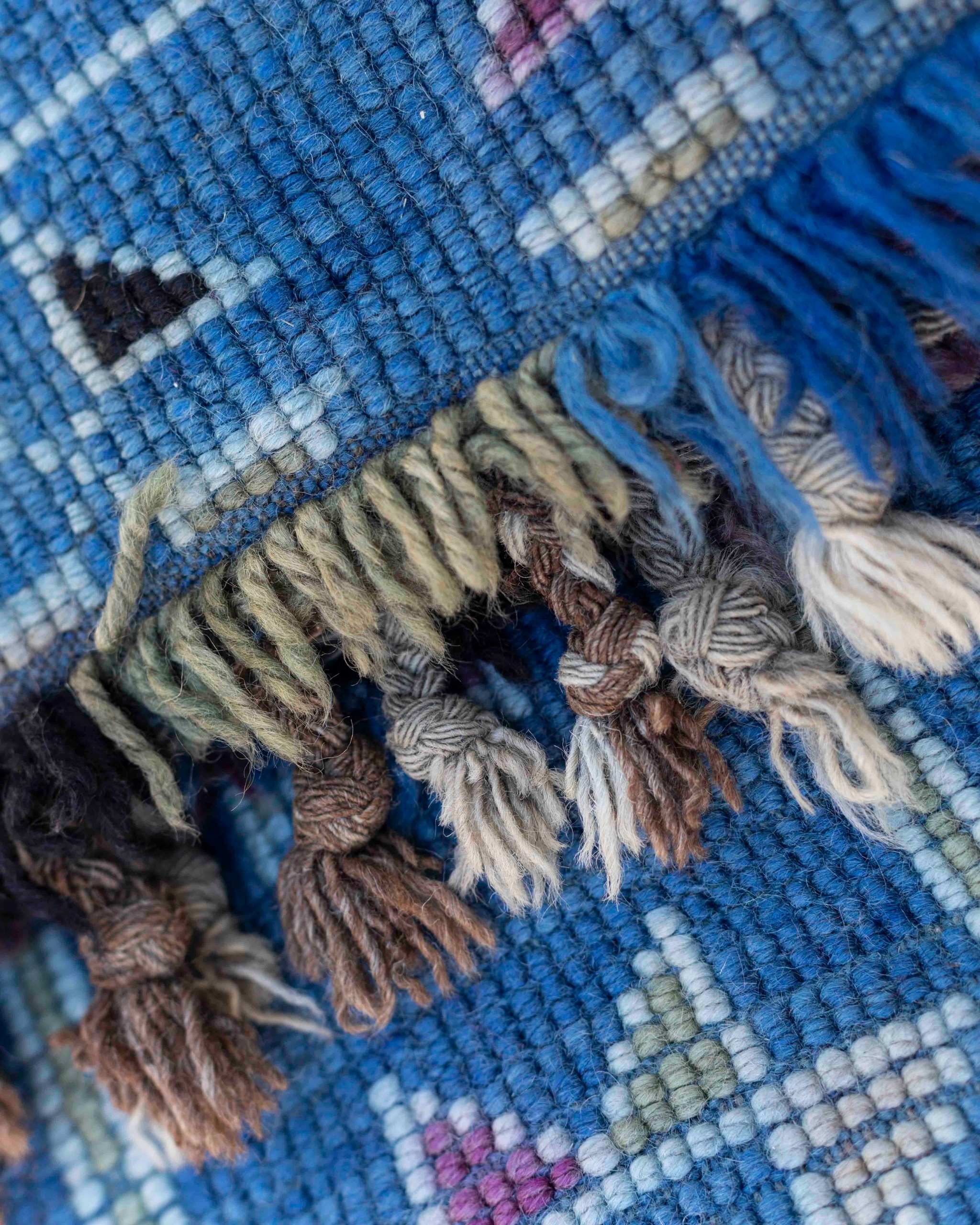 Dettaglio del retro del tappeto blu con simboli policromi e delle frange corte