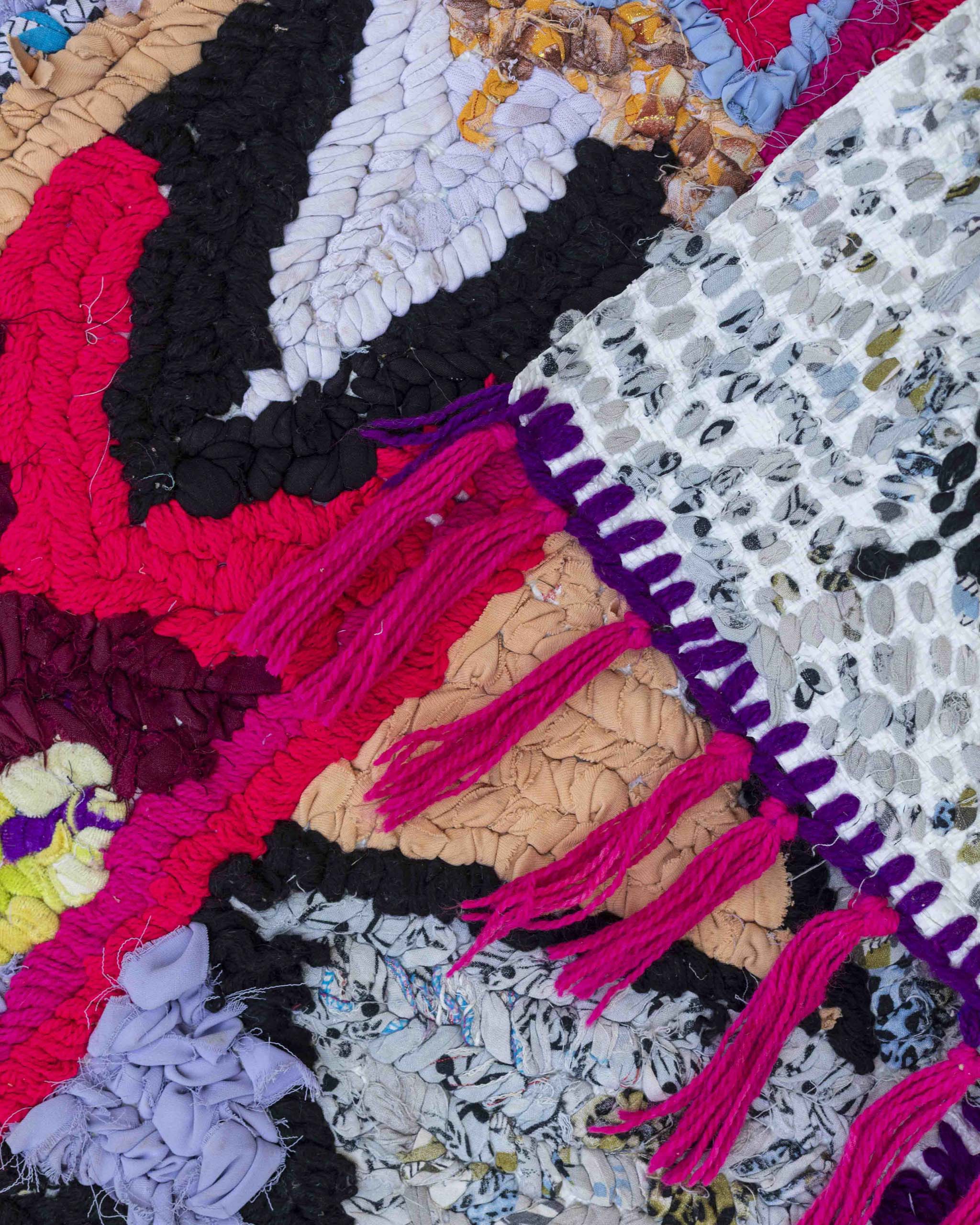 Dettaglio fronte-retro e frange del tappetino in strisce di tessuti misti annodati su un sacco di plastica riciclato