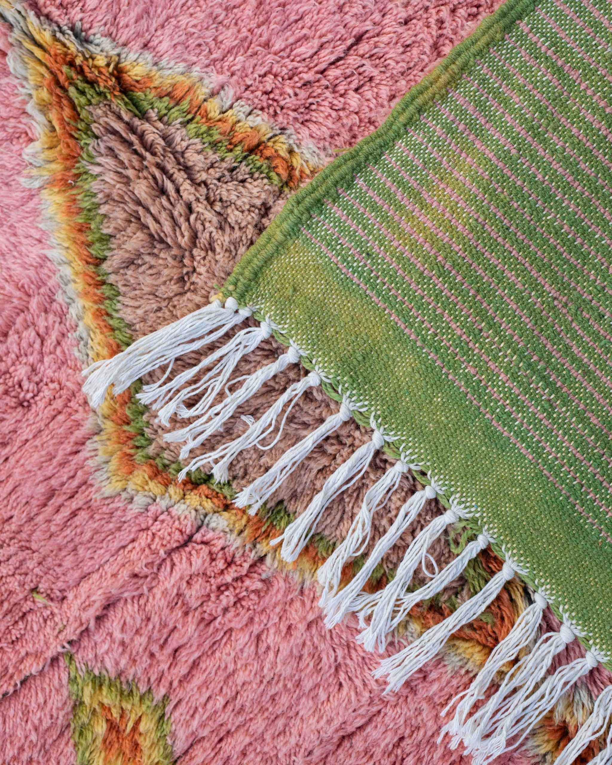 Dettaglio fronte retro del tappeto annodato a mano in lana rosa e verde, con dettagli in arancione, giallo, bianco