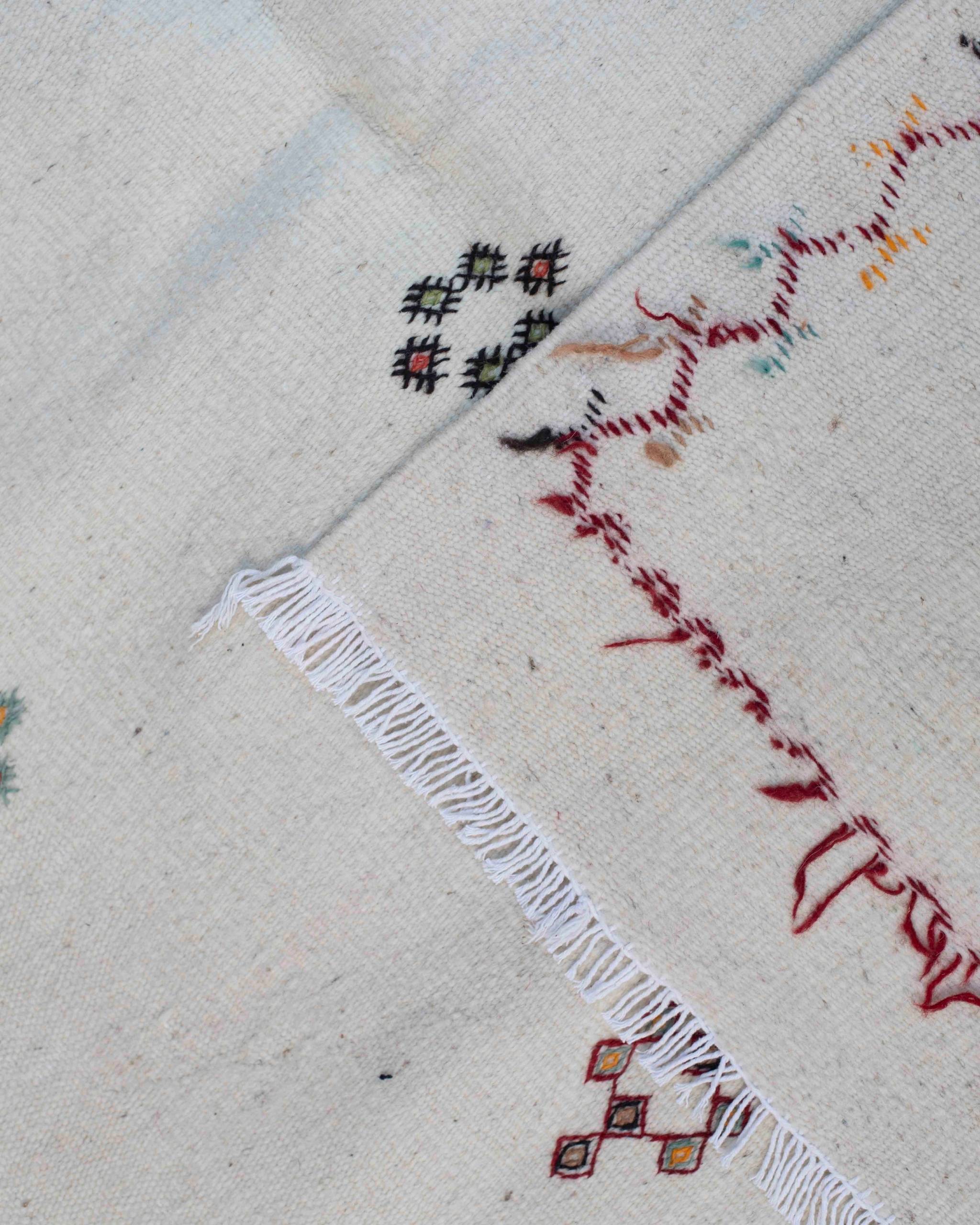 Dettaglio frange e bordo ricamato del tappeto Akhnif in lana a tessitura piatta, con zigzag e micro-motivi geometrici