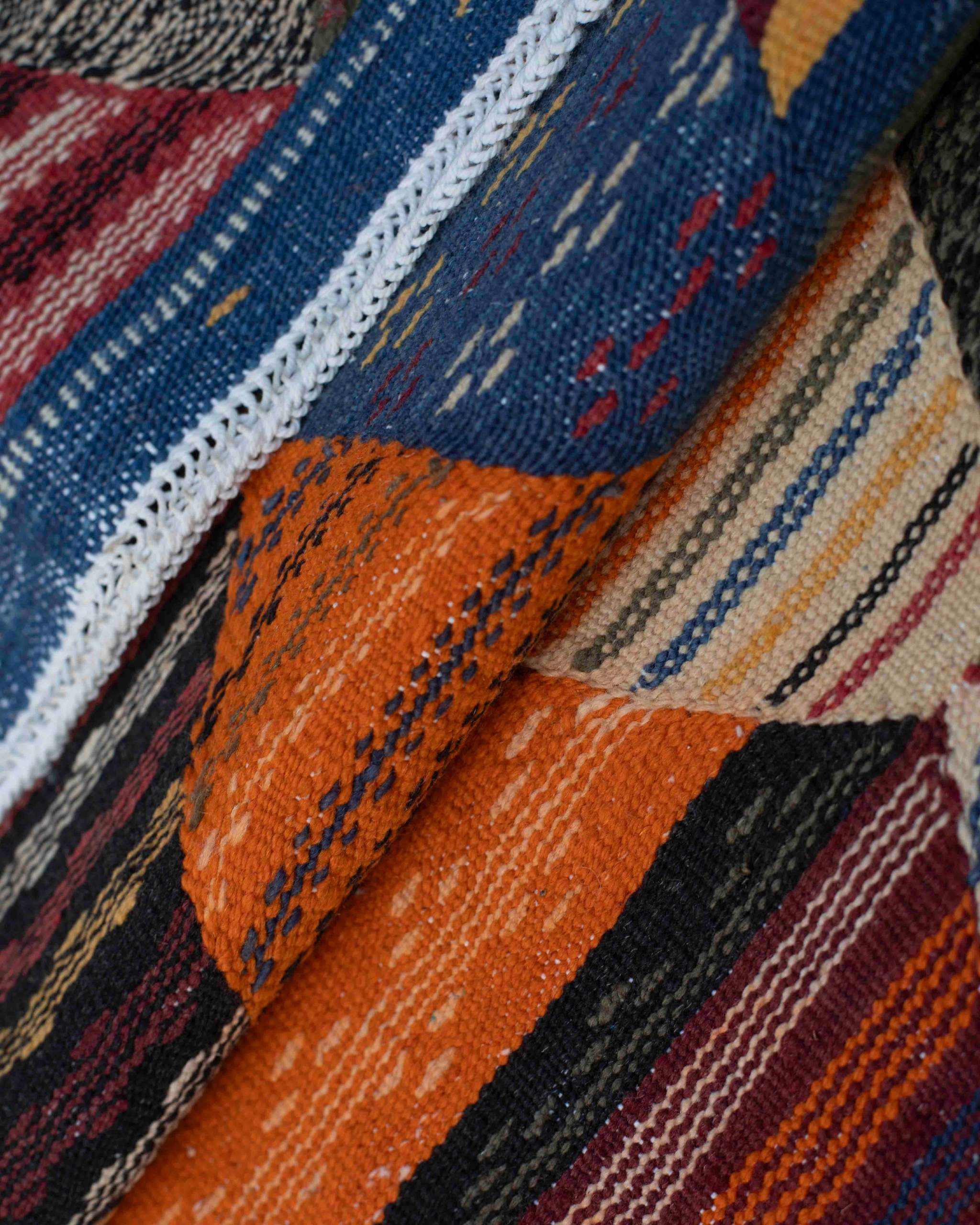 Dettaglio tessitura piatta della passatoia Kharita in lana: trama fitta, righe multicolore e bordo blu con bordatura intrecciata