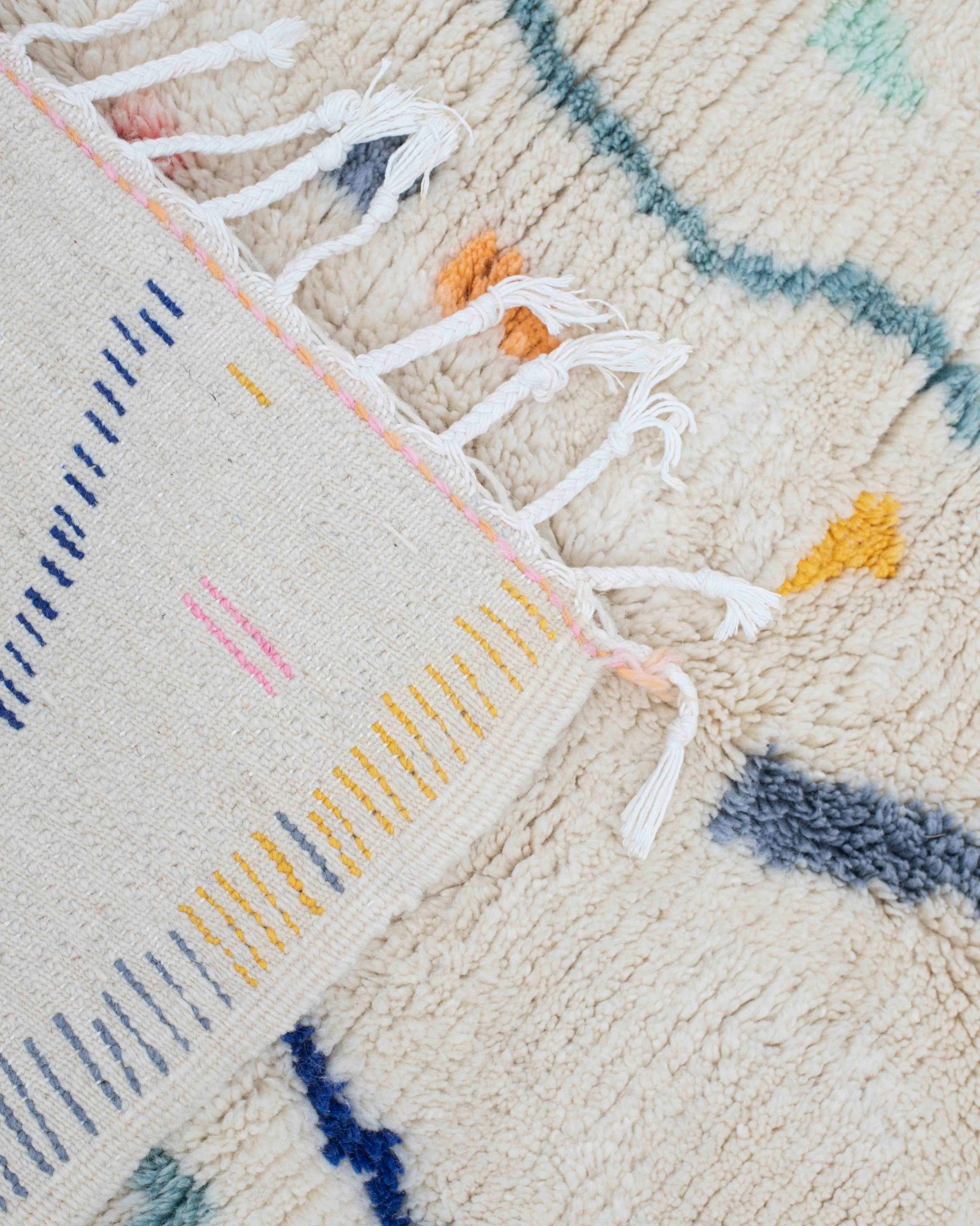 Dettaglio del rovescio e delle frange bianche del tappeto Azilal bianco con segni grafici blu, gialli, arancioni e rosa
