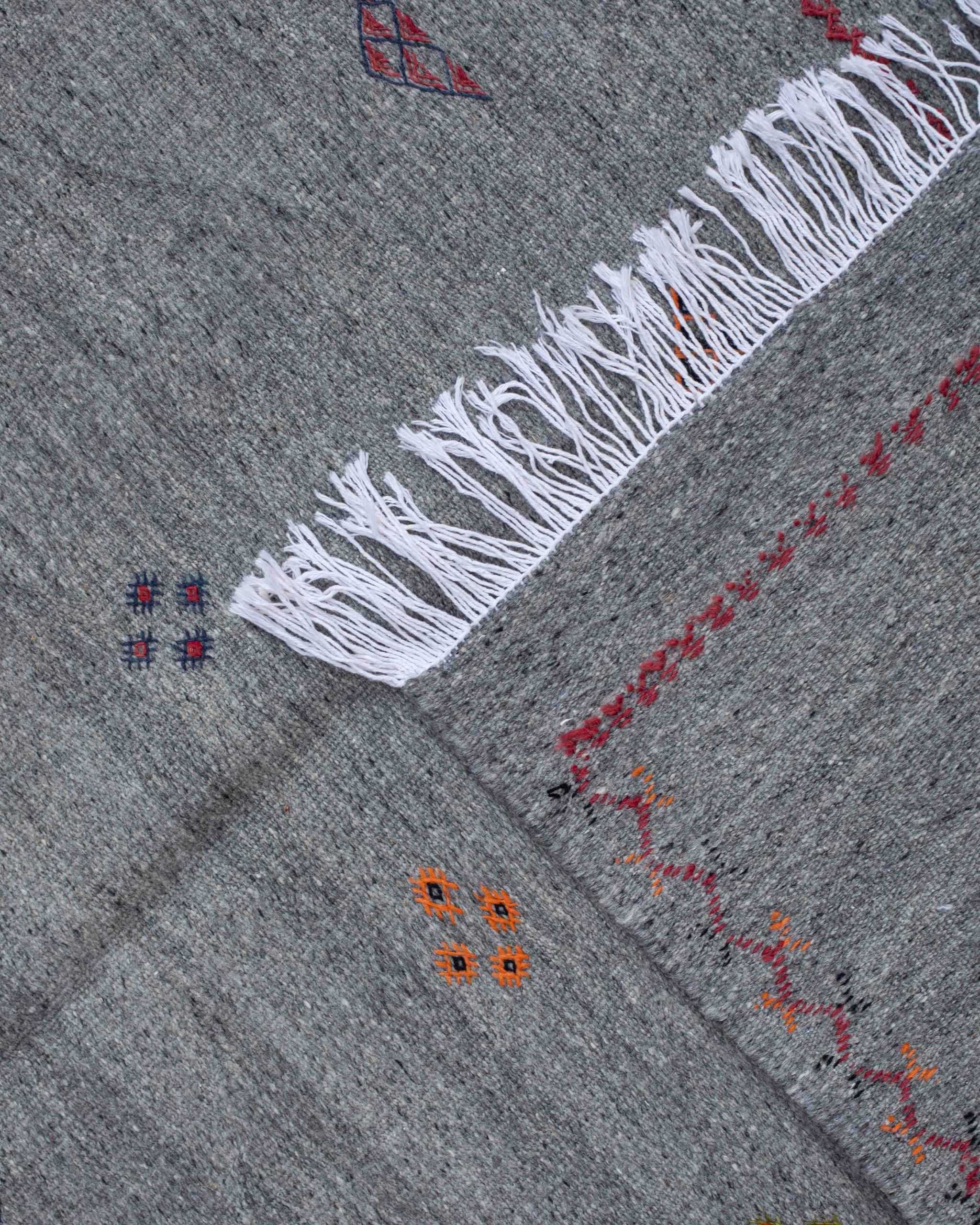 Frange bianche e piccoli ricami geometrici su tappeto kilim Akhnif grigio a tessitura piatta
