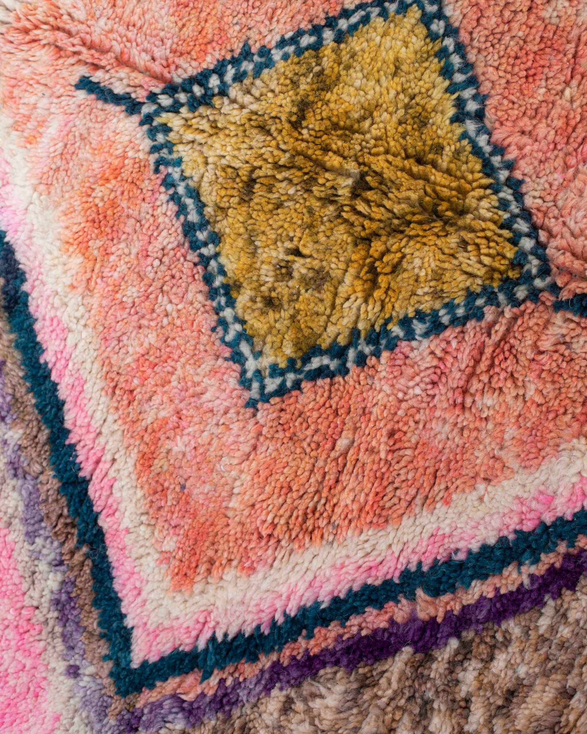 Dettaglio di un rombo ocra-marrone e rosa-corallo con bordi blu, rosa e viola, del tappeto Beni Ourain con effetto abrash della lana