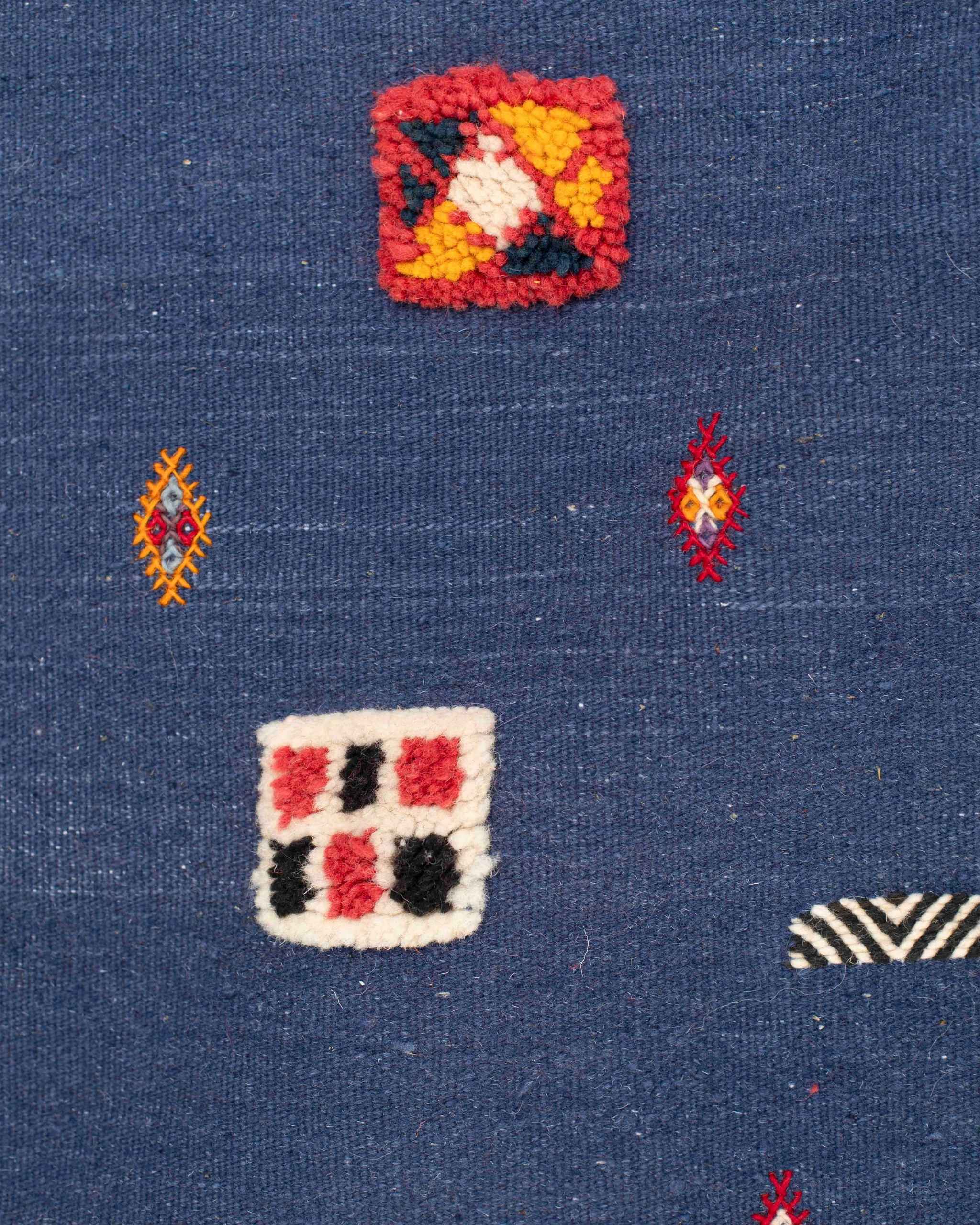 Dettaglio dei simboli berberi e dei decori rossi, gialli, bianchi e neri sul tappeto kilim blu Kharita