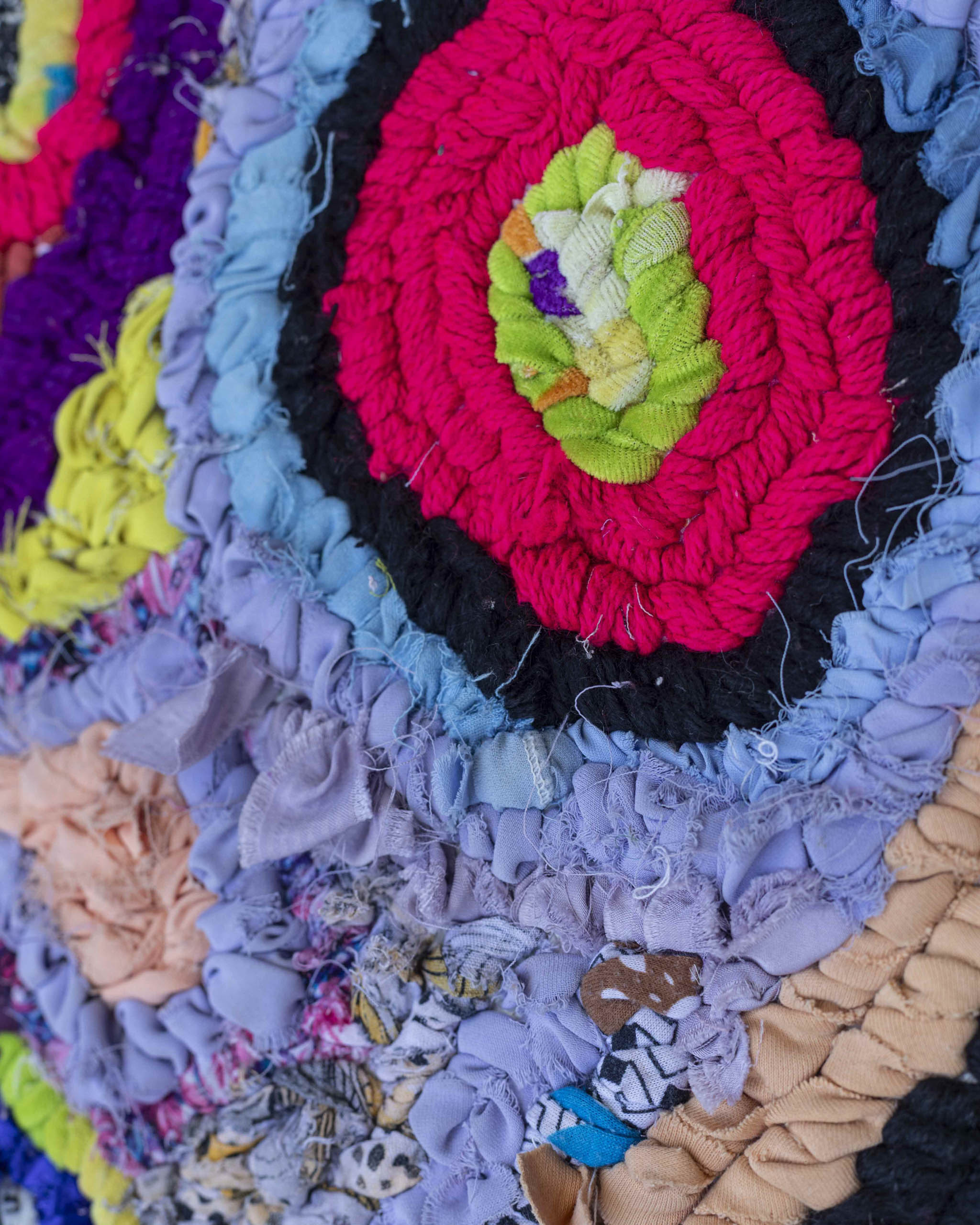 Dettaglio di un cerchio lilla, azzurro, nero, fucsia, verde, su tappetino di stracci