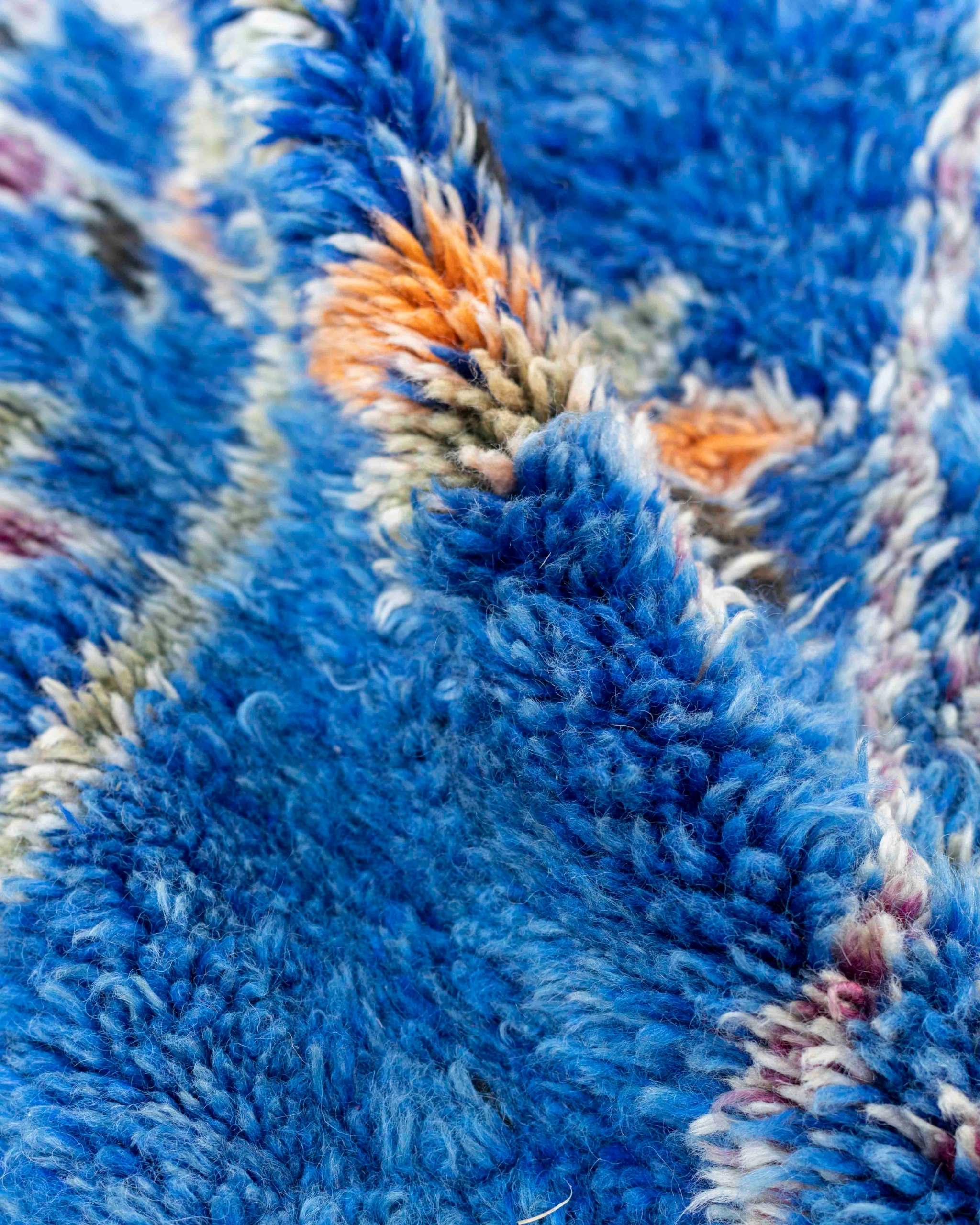 Dettaglio del tappeto blu a pelo medio-lungo con fantasie geometriche arancioni, verdi, viola