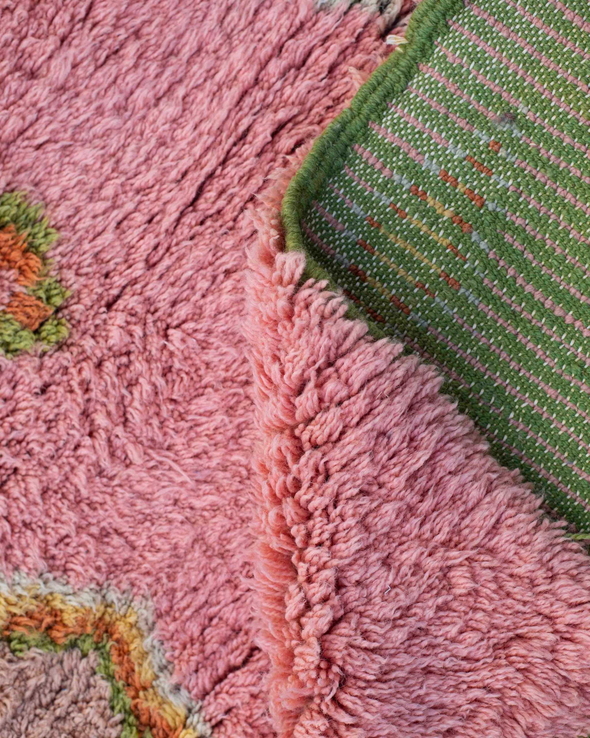 Dettaglio fronte retro del tappeto annodato a mano in lana rosa e verde con dettagli colorati
