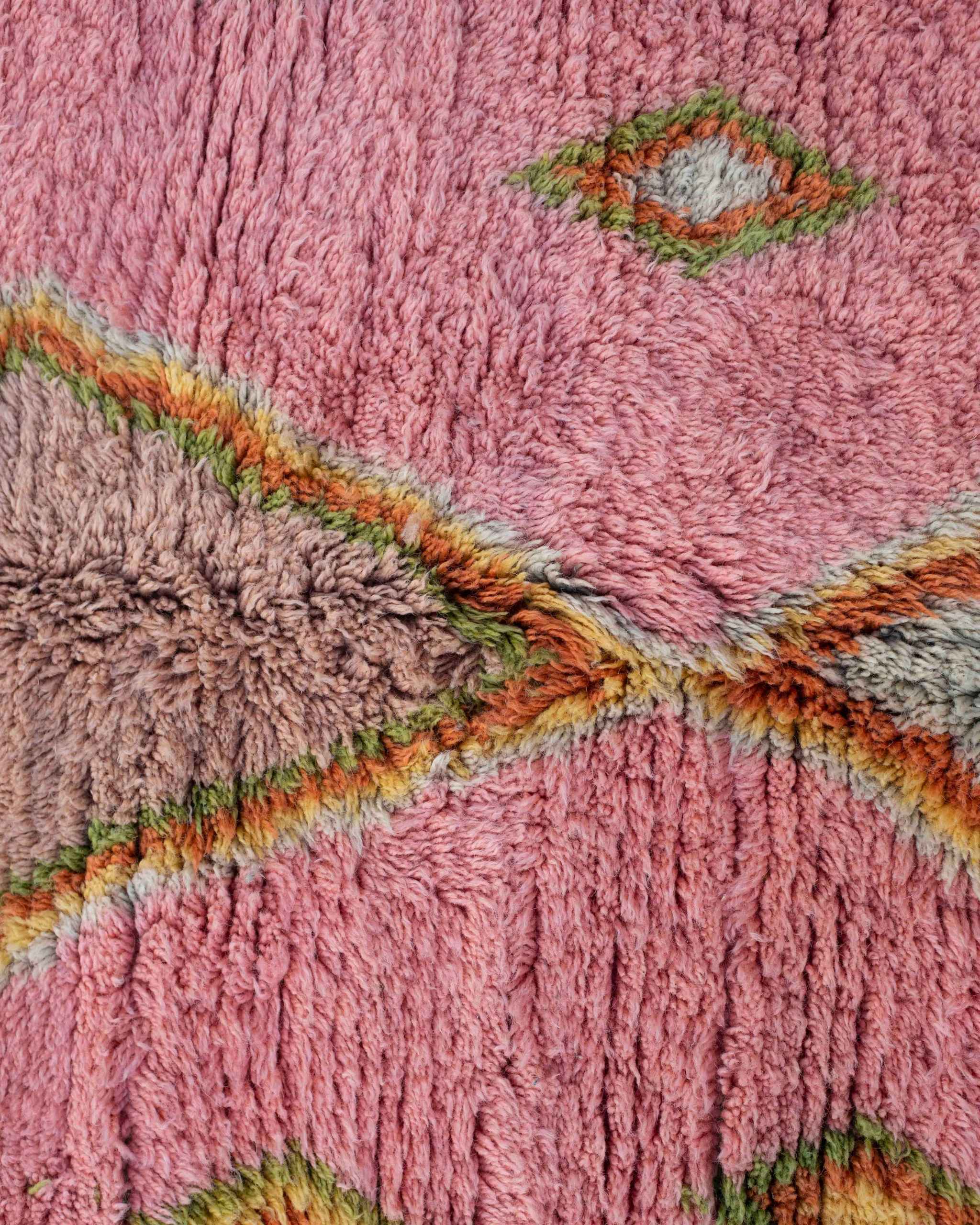 Dettaglio delle losanghe a rombi centrali del tappeto rosa con simboli geometrici in verde, arancione, cipria