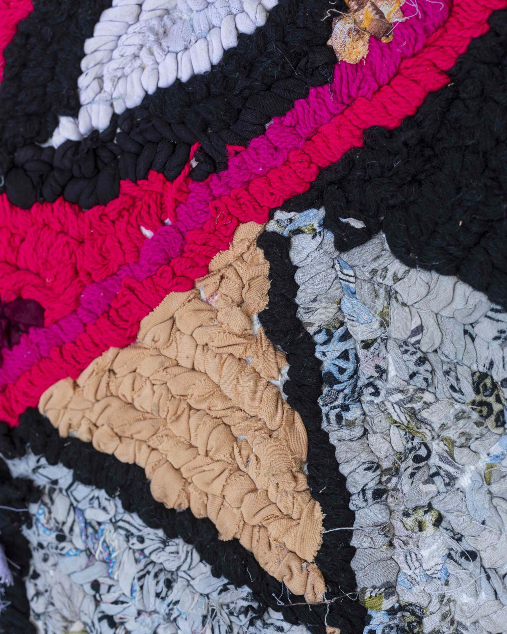 Dettaglio di una porzione del tappetino in stoffe riciclate con fantasia a triangoli e righe in grigio, azzurro, nero, cipria, fucsia, magenta