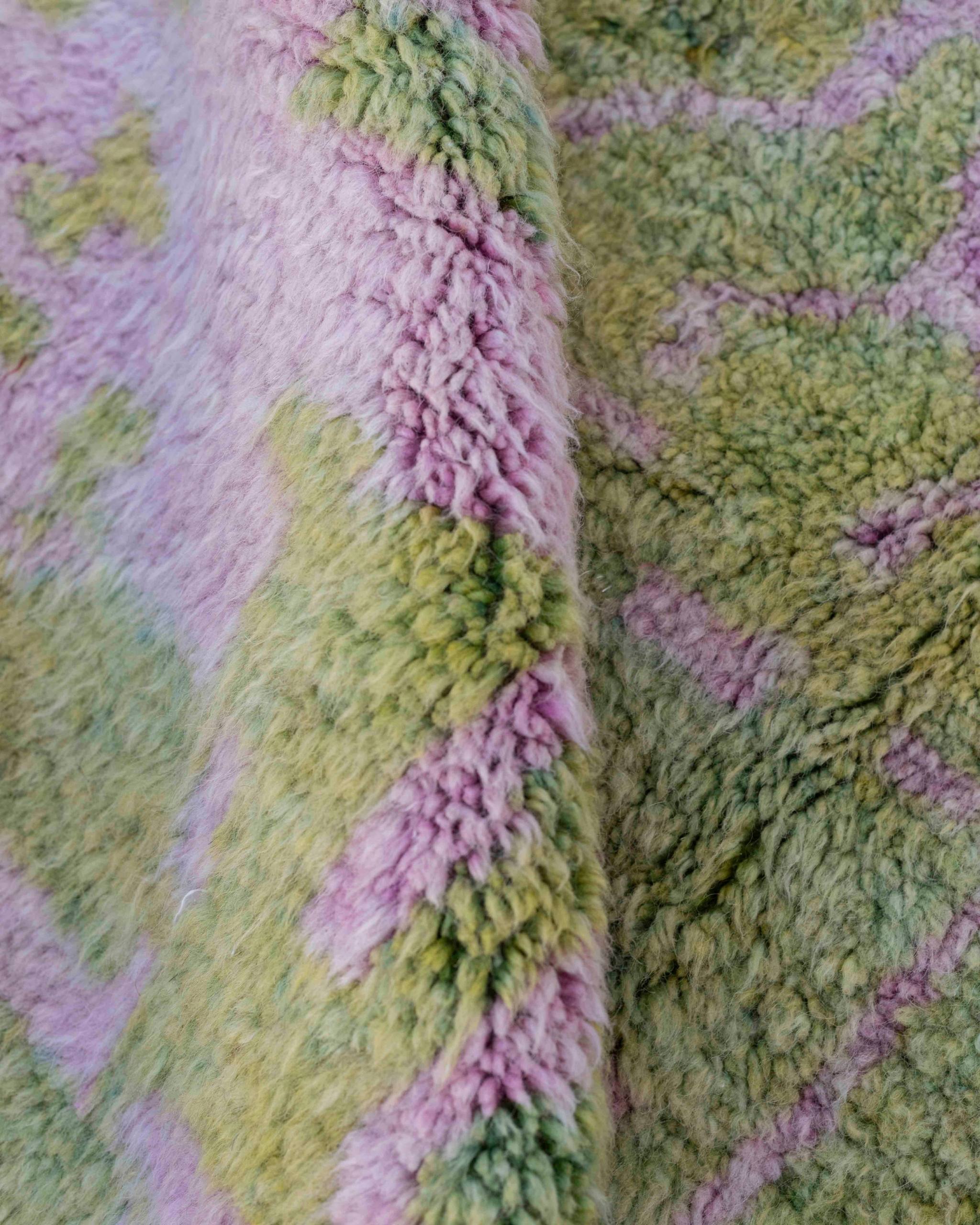 Dettaglio del pelo del tappeto in lana con sfumature verdi e rosa sorbetto dove è visibile l'abrash