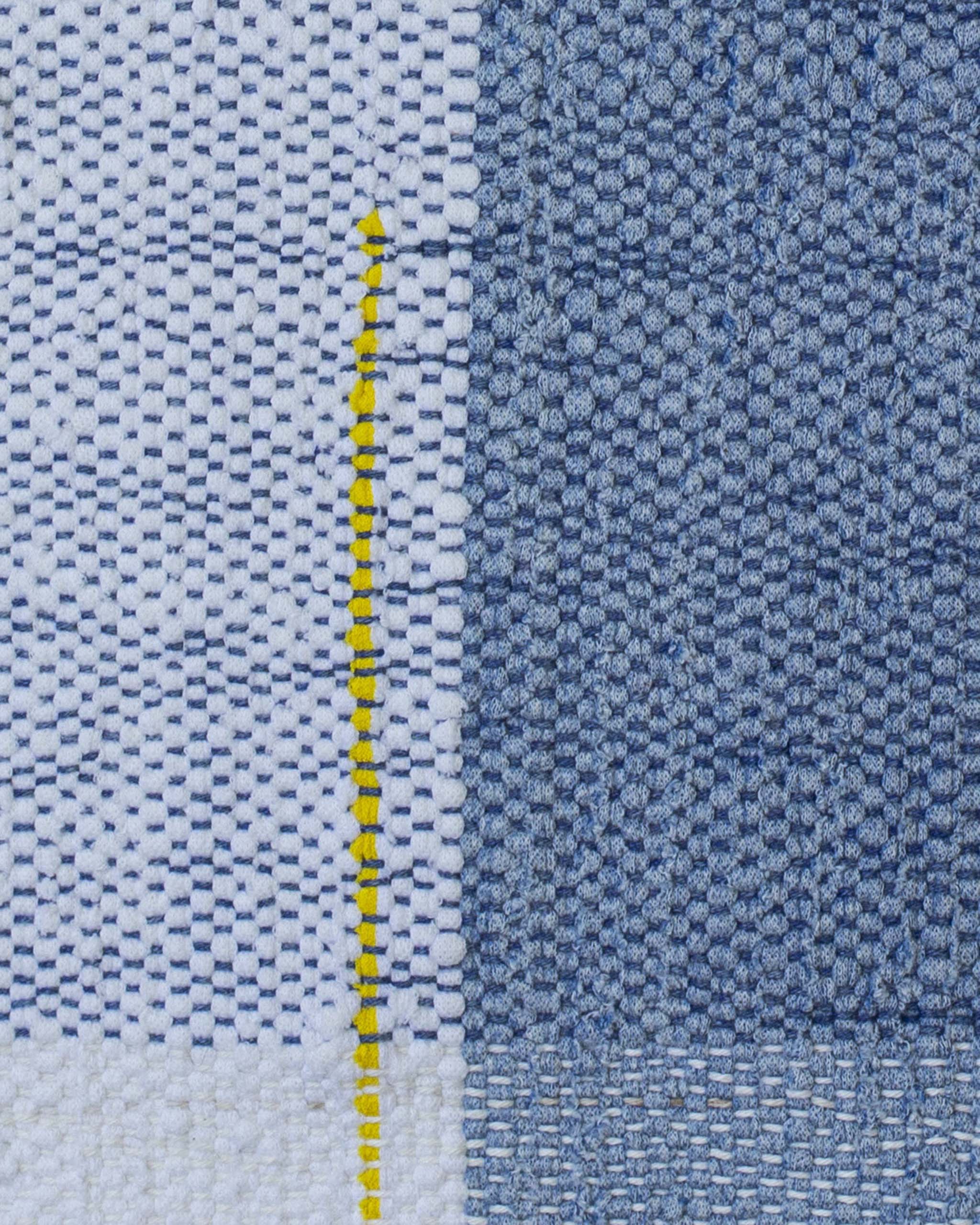 Dettaglio della federa del cuscino tessuta a mano in filati bianchi, blu, azzurri, con linea singola gialla