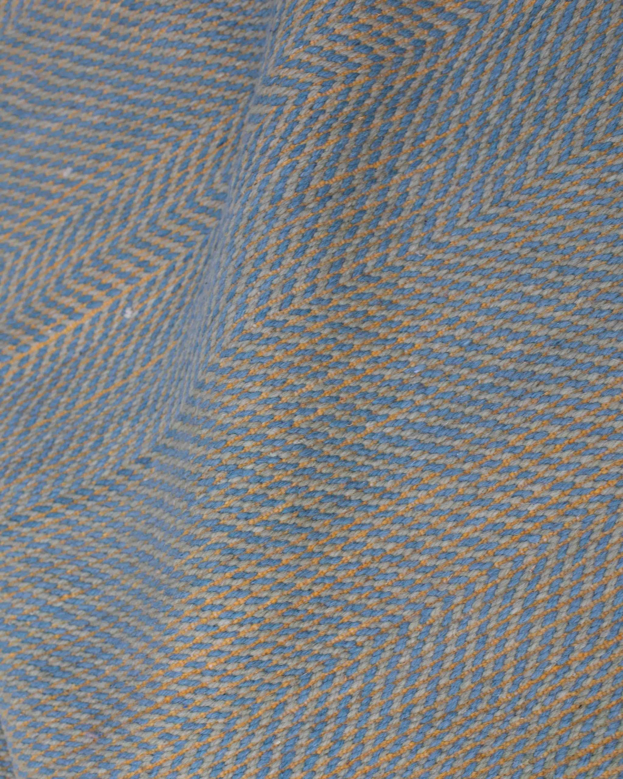 Dettaglio della tessitura piatta del tappeto Zanafi in lana: motivo chevron tono su tono con intreccio azzurro e giallo
