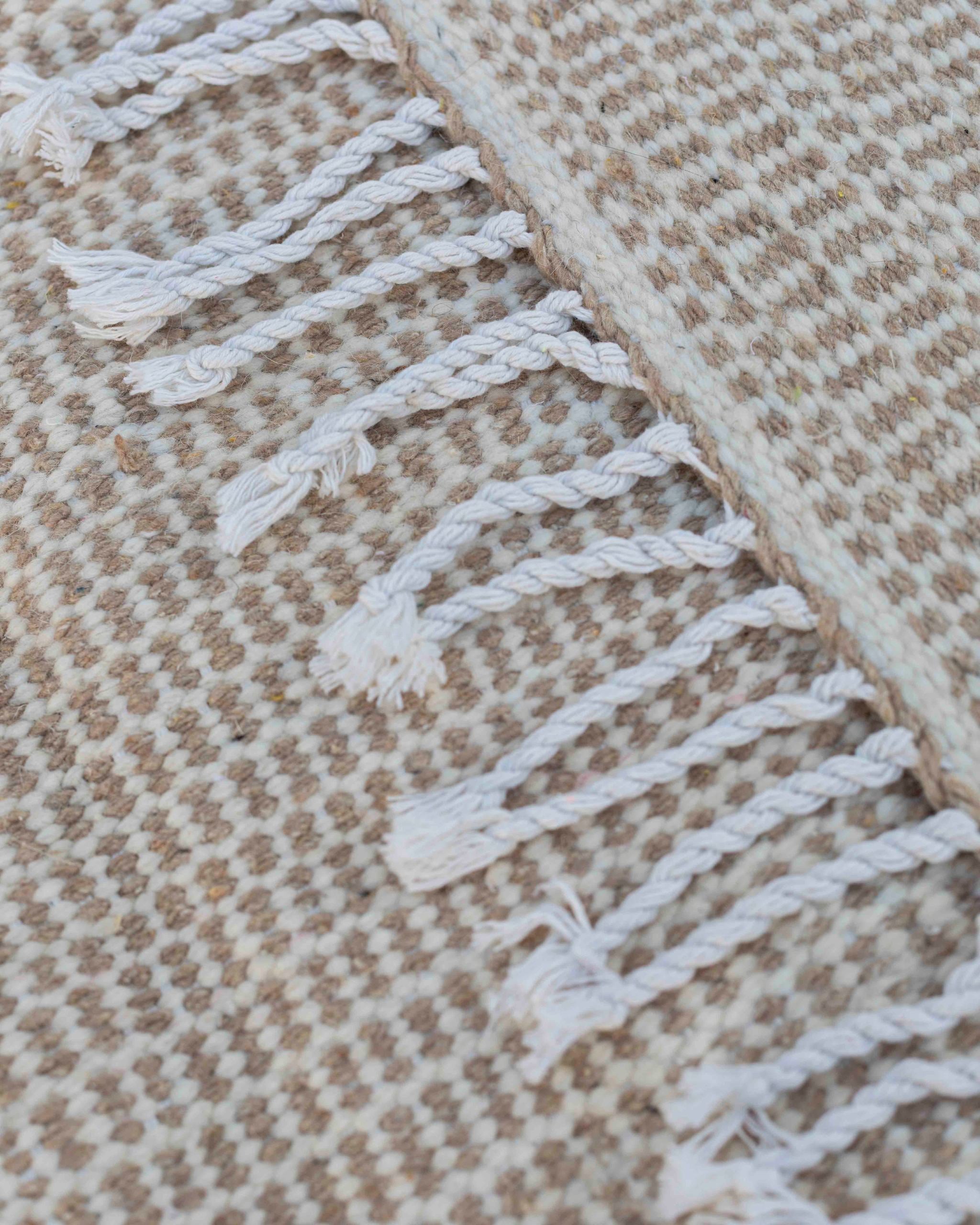 Dettaglio della trama compatta e delle frange del tappeto Hanbel beige e bianco in lana