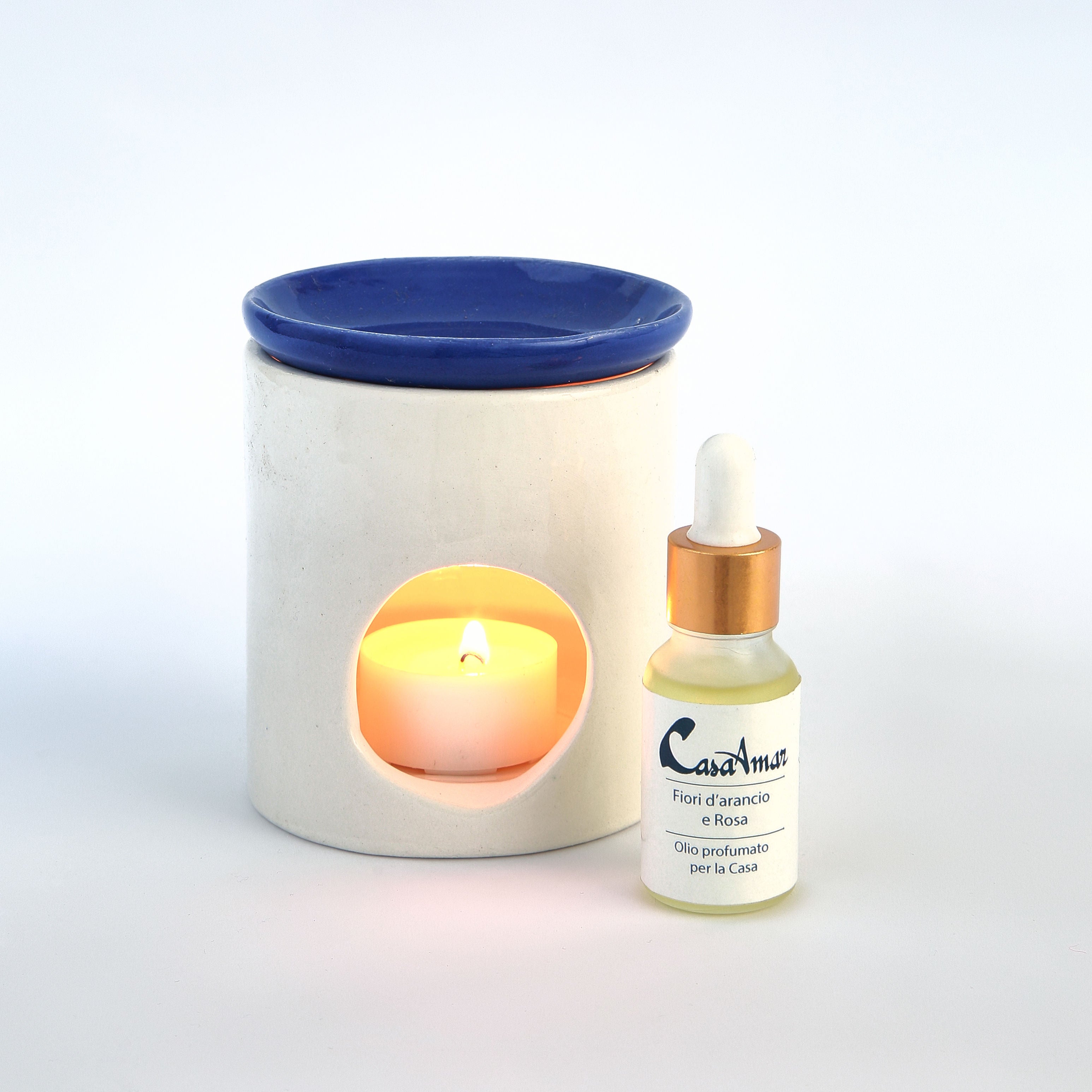 diffusore in ceramica con una candela all'interno e piattino blu, a fianco una boccettina di olio profumato