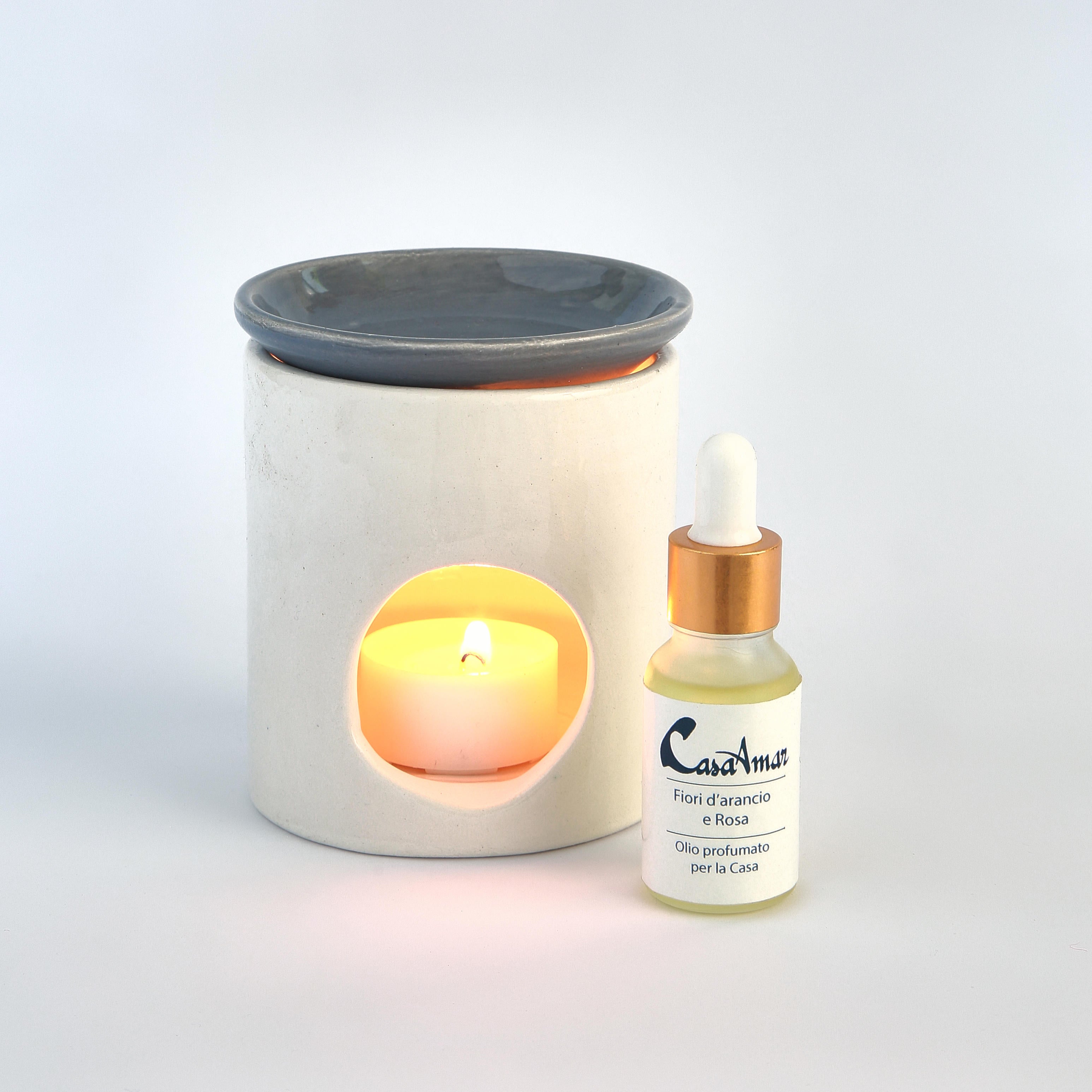 diffusore in ceramica con una candela all'interno e piattino grigio, a fianco una boccettina d di olio profumato