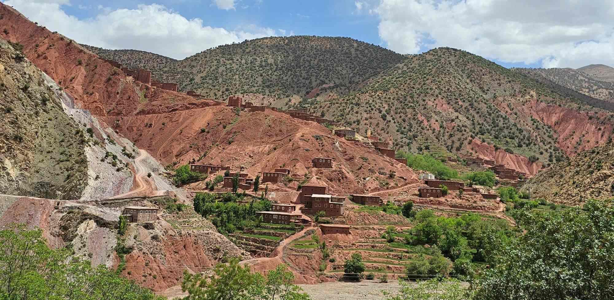Picturesque Amazigh Berber village nestled in Morocco's Atlas Mountains, traditional red clay houses amid rugged terrain - backdrop for authentic Moroccan Berber rug craftsmanship