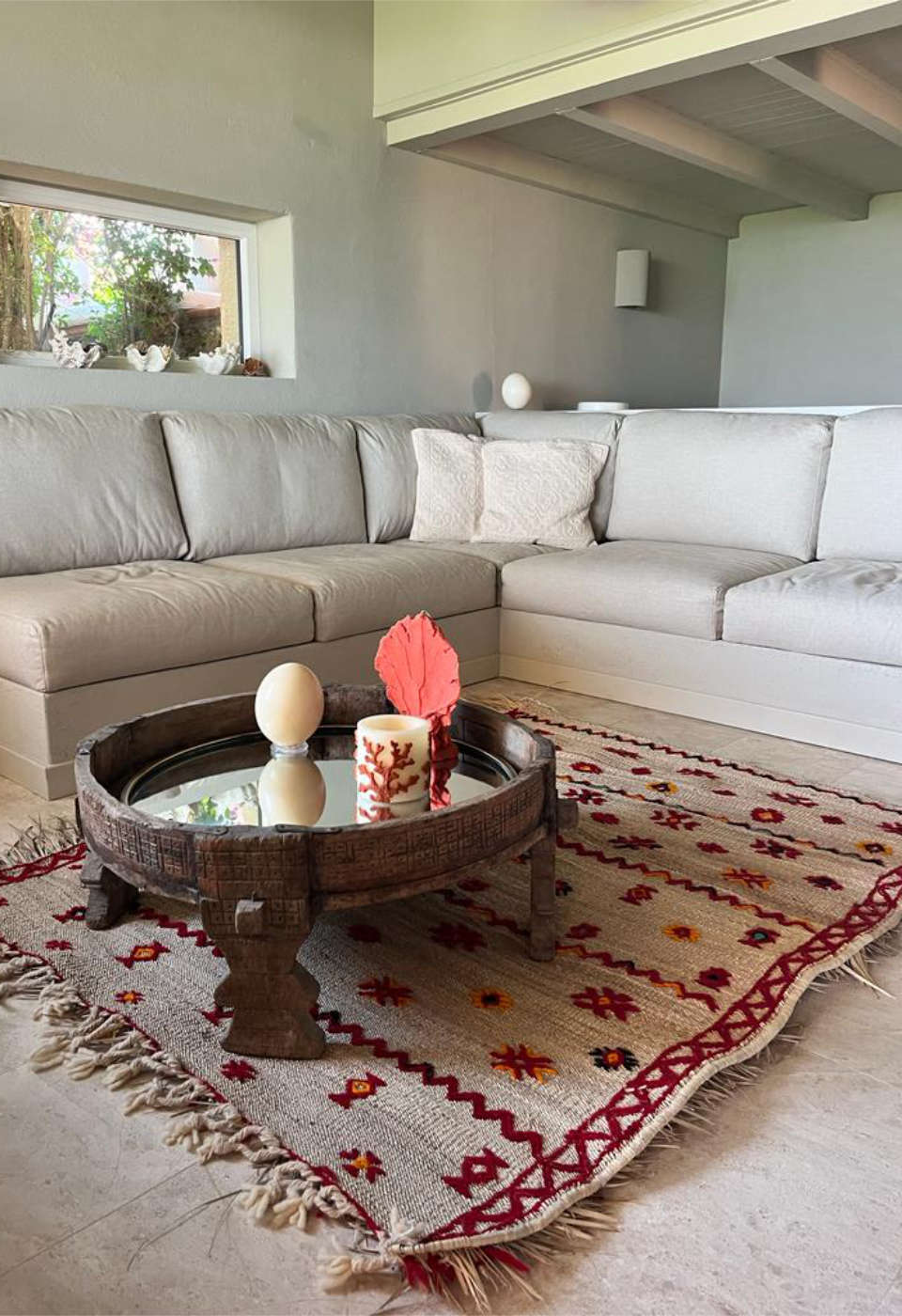 Authentic Moroccan straw mat with red and orange floral patterns in a contemporary living room, paired with a beige sectional sofa and rustic wooden coffee table