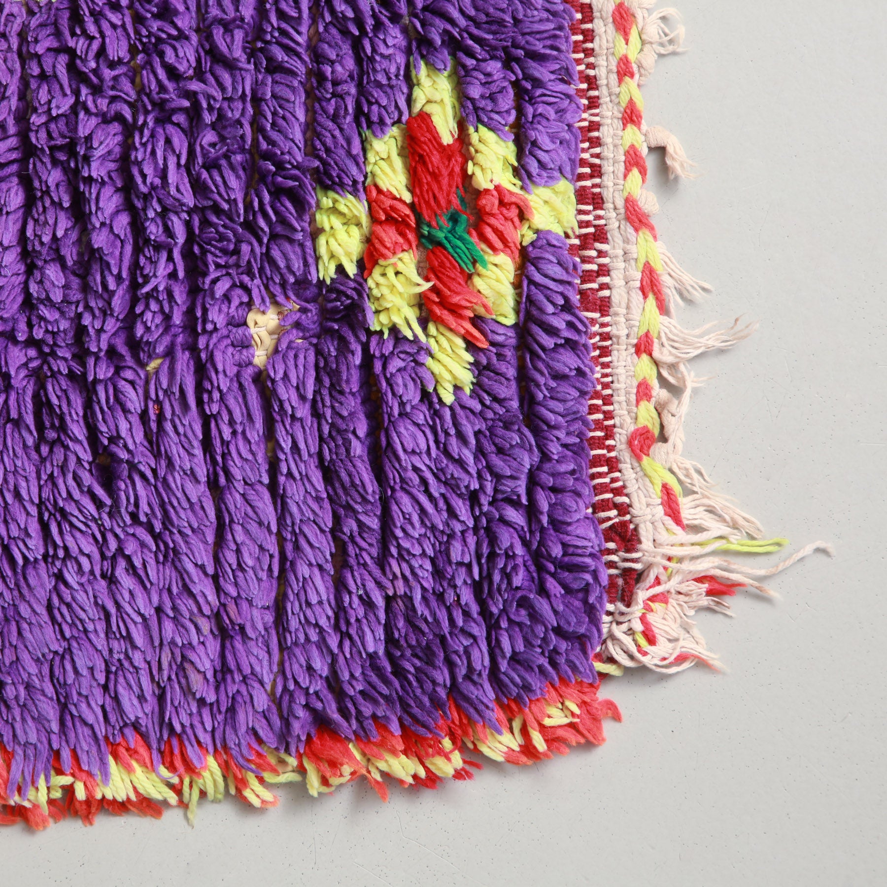 angolo di un tappeto boucherouite realizzato annodando lana e vecchi  tessuti, base viola con cornice gialla e rossa e piccolo rombo realizzato con quadrati gialli rosso e verde