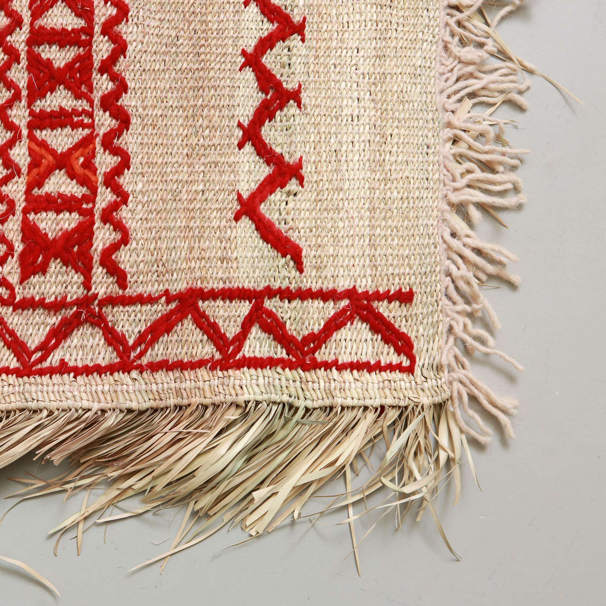 angolo e frangia di una stuoia in paglia realizzata a mano in marocco con motivi geometrici a zig zag gemotrtrici in lana rossa