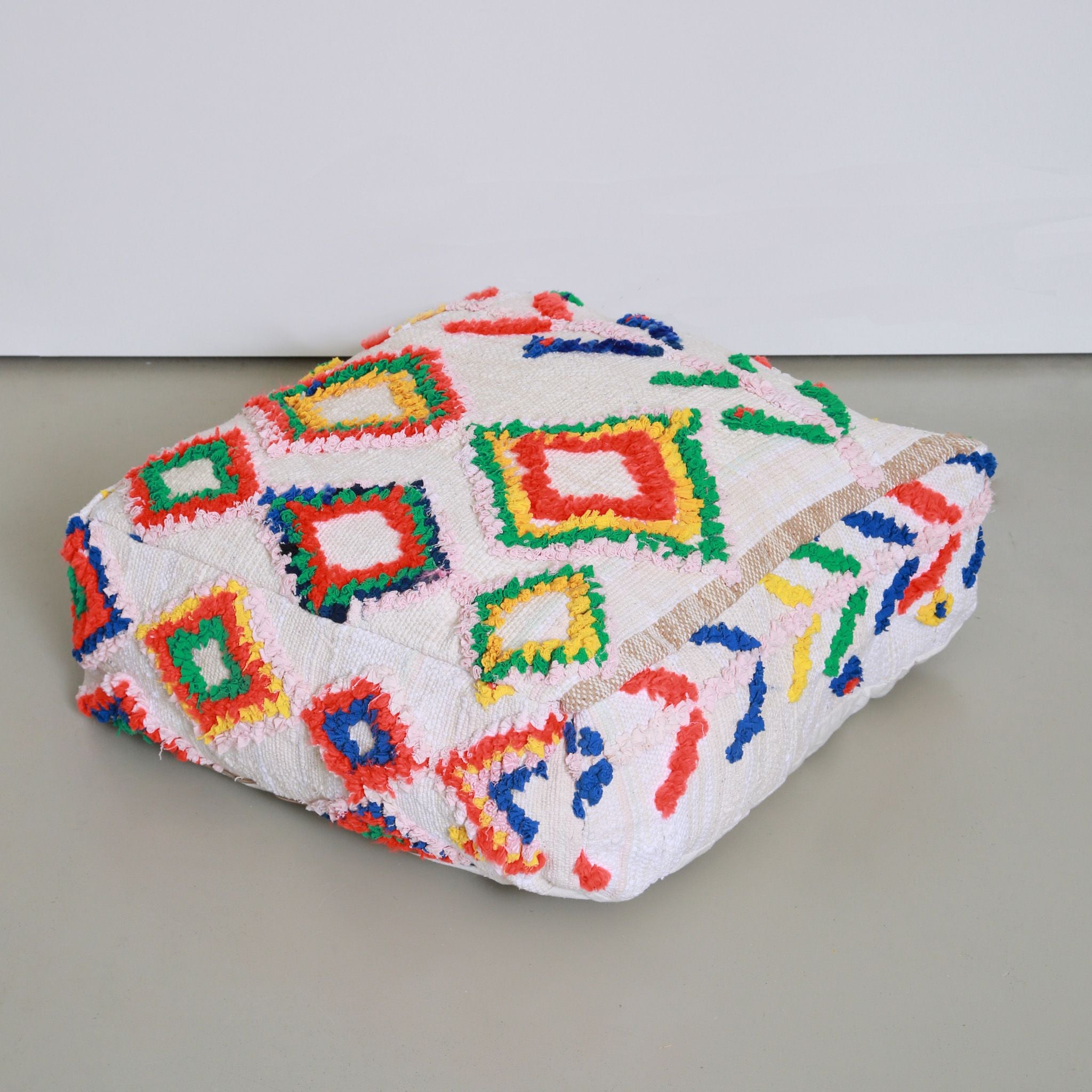 Pouf marocchino Boucherouite bianco con motivi geometrici colorati in rosso, verde, blu e giallo, realizzato con tessuti riciclati
