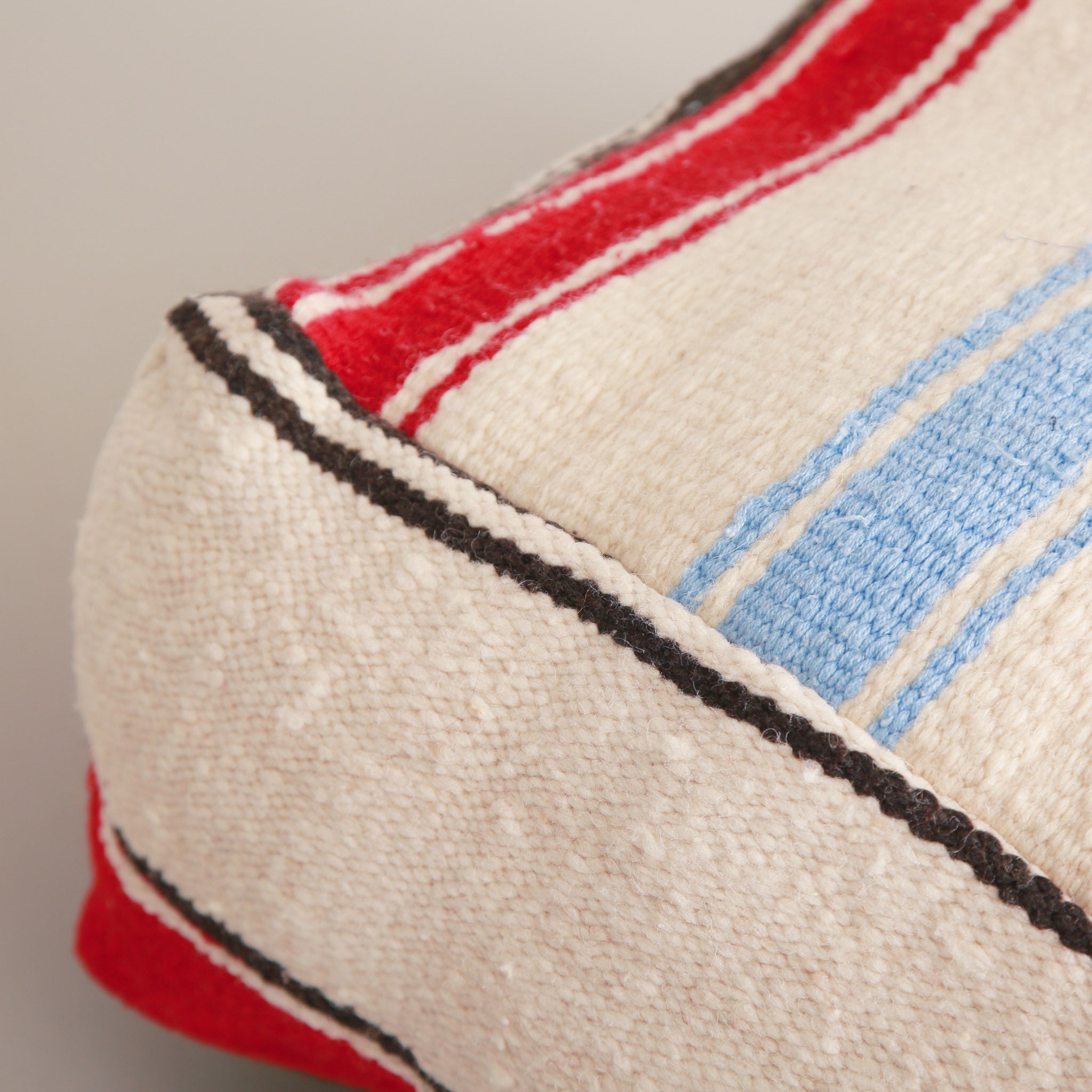 angolo di un Pouf marocchino quadrato realizzato con coperta vintage in lana, con motivo a strisce colorate bianche, rosse, verdi e azzurre su sfondo chiaro