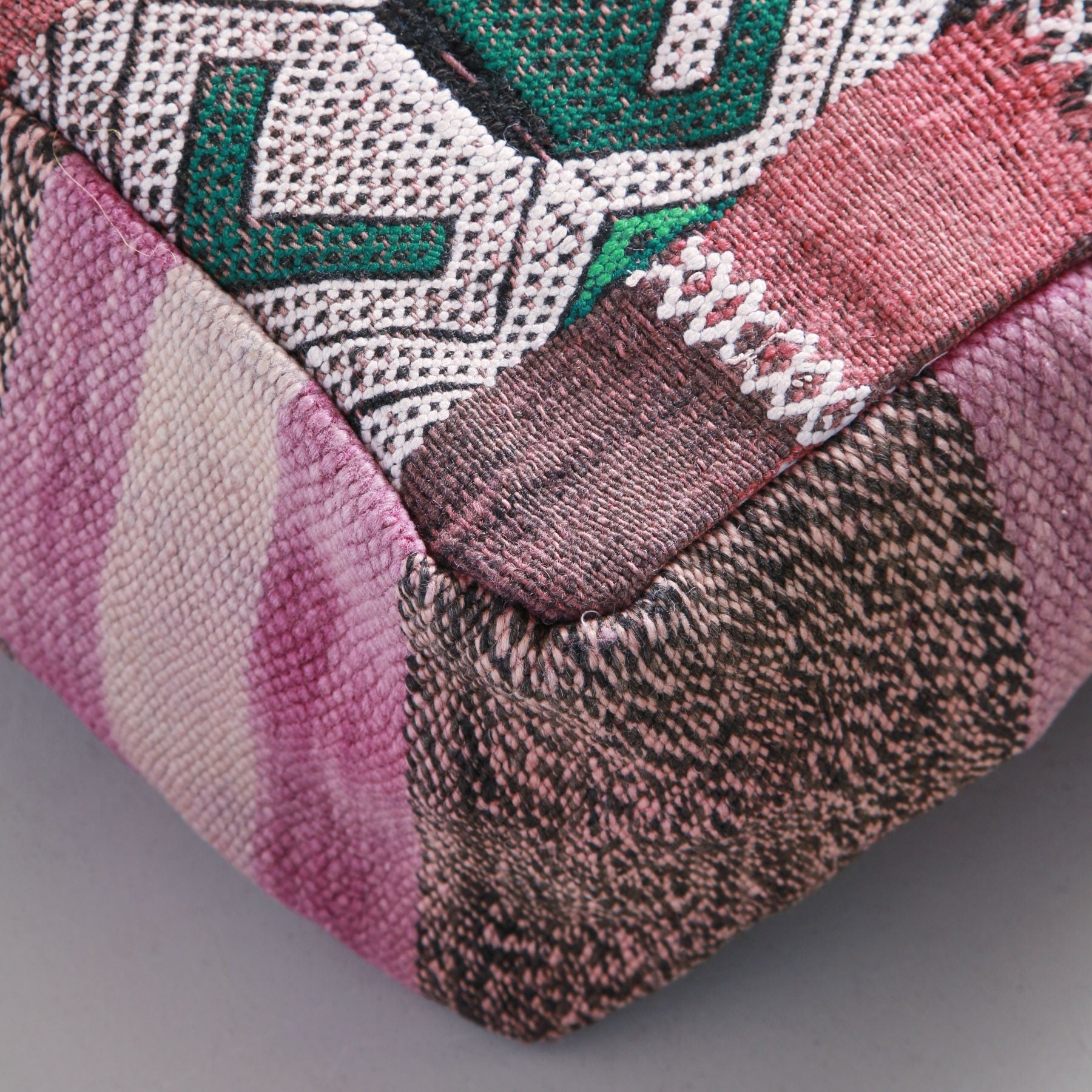 angolo di un pouf ricavato da un tappeto marocchino vintage in lana dalle tonalità di rosa con ricamo bianco e verde