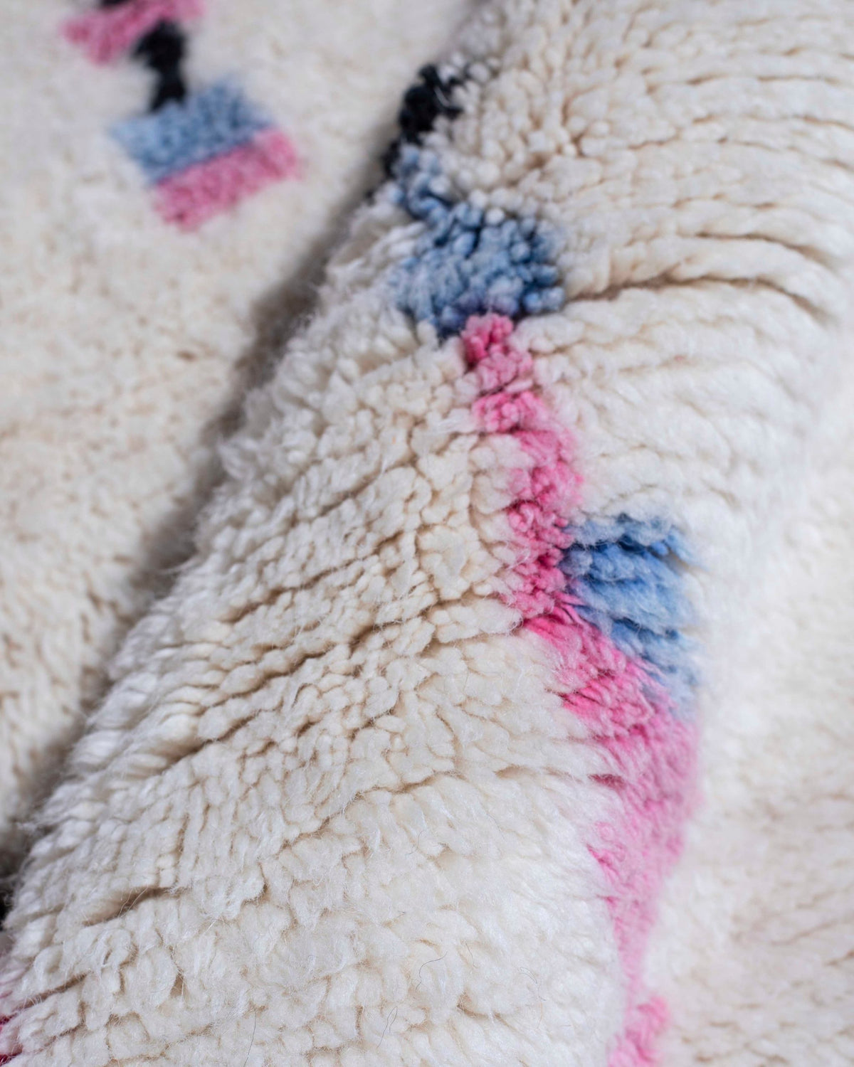 Dettaglio dei segni rosa e azzurri pastello su fondo bianco del tappeto Azilal in lana