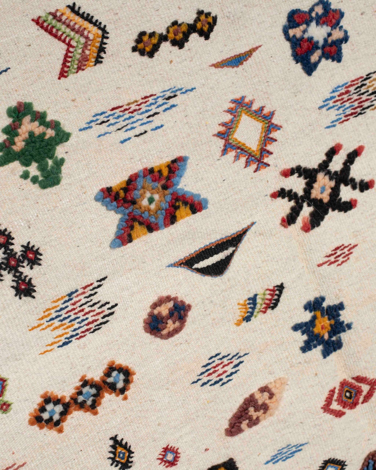 Dettaglio dei simboli berberi colorati sul fondo in lana écru del tappeto kilim marocchino Taznakht