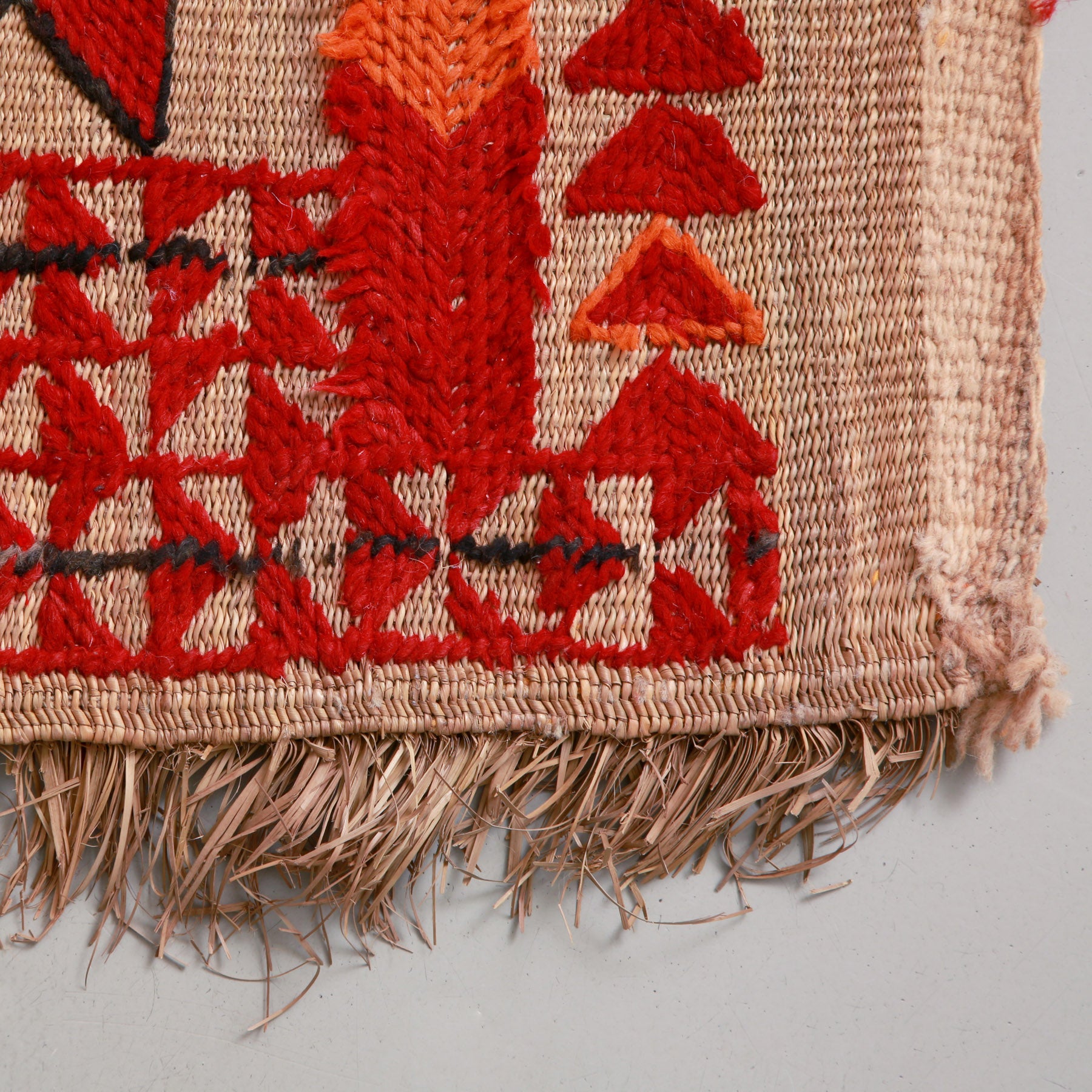 angolo di una stuoia in paglia di palma con ricami in lana rossa arancione e nera