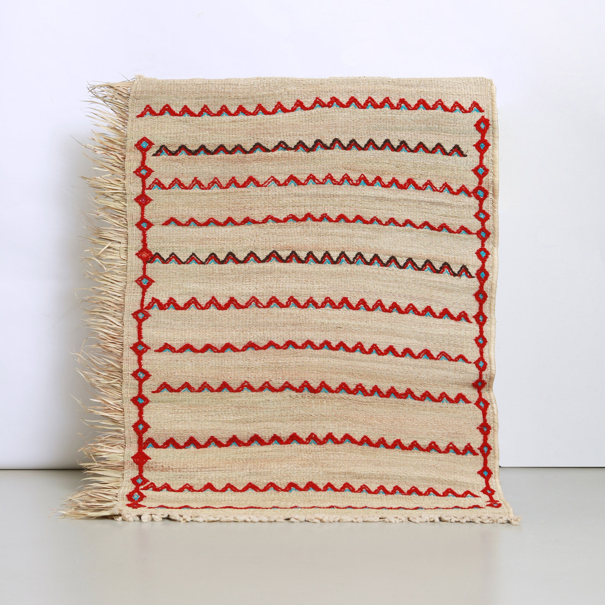 visione completa di una stuoia in paglia hassira con ricami geometrici a zig zag in lana rossa e zaaurra con accenni di nero e pattern a rombi sui lati