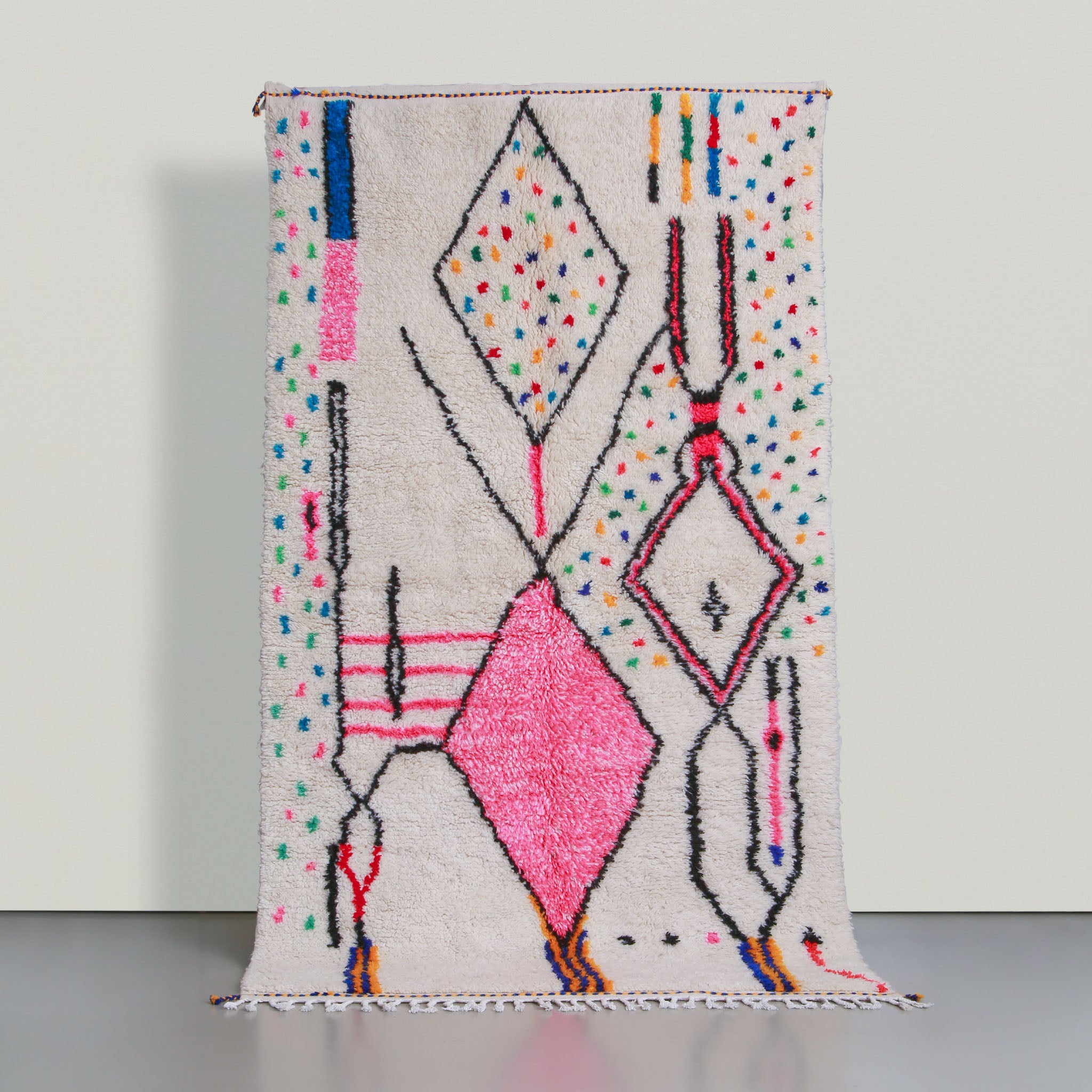 tappeto marocchino stile azilal con base in lana bianca e simboli con contorni neri tre grandi rombi di cui uno con interno rosa e pois blu gialli rossi e verdi
