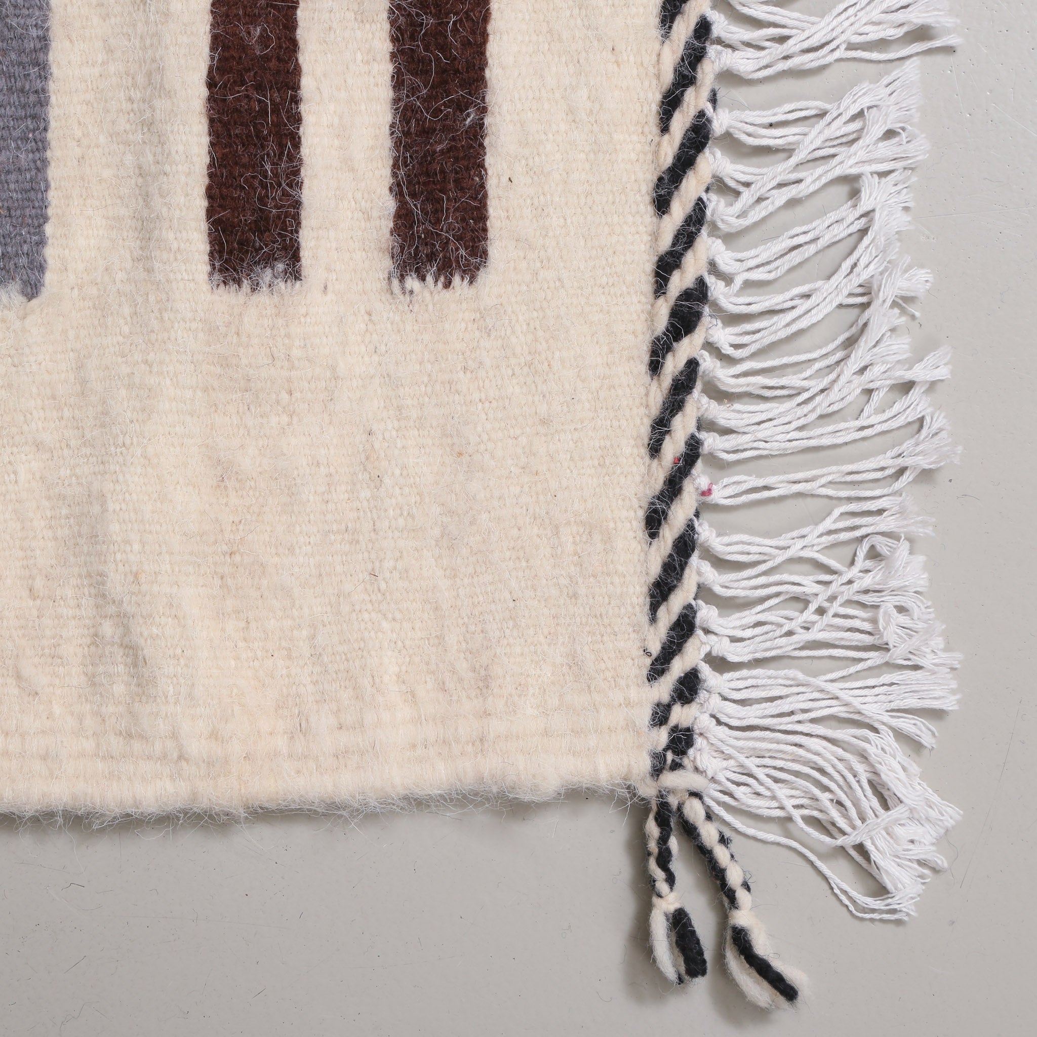 angolo di un tappeto azilal a tessitura piatta in lana color panna con bordo prima della frangia a righe diagonali bianche e nere